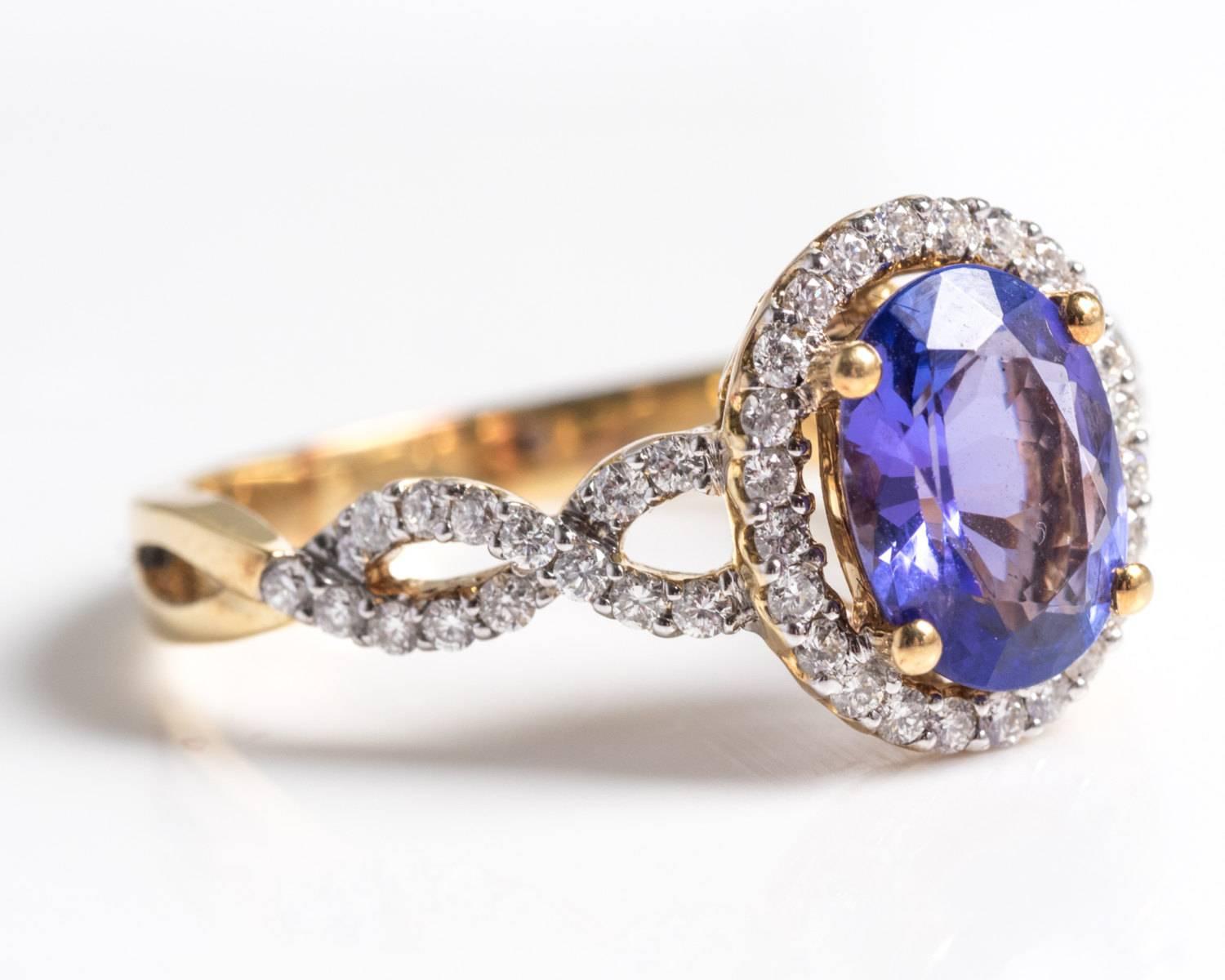 This tanzanite ring is beaming with color and sophistication. 
This bright purple oval cut tanzanite is mounted in its four-prong yellow gold frame. There is a halo of twenty-four diamonds surrounding the center stone. 

Underneath this cluster