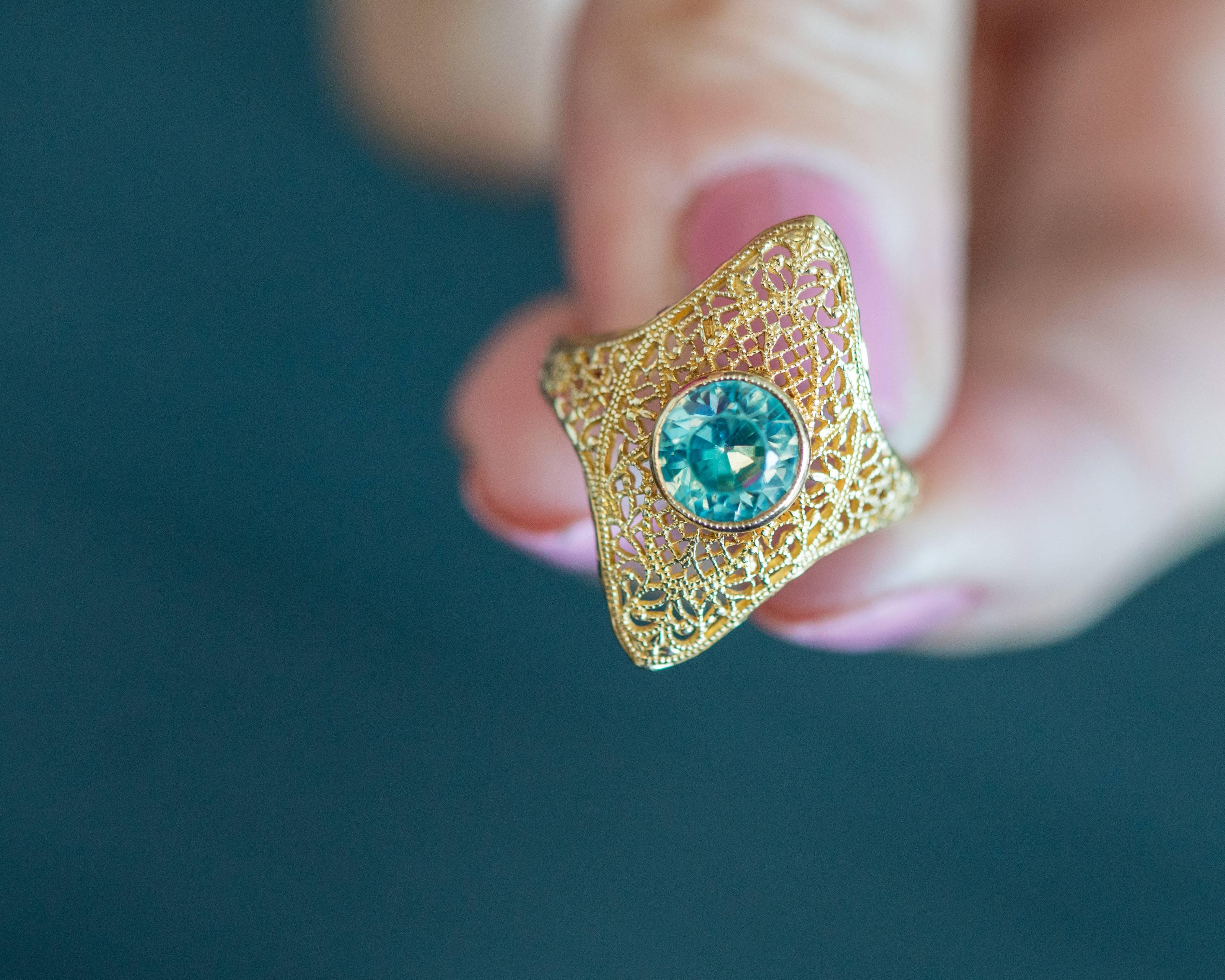 This 1940s Natural Blue Zircon ring features a 1.25 carat clear light blue zircon center stone bezel set in a richly hued 14 karat yellow gold which also comprises the marquise shaped filigree head and shoulders of the ring. This timeless ring will
