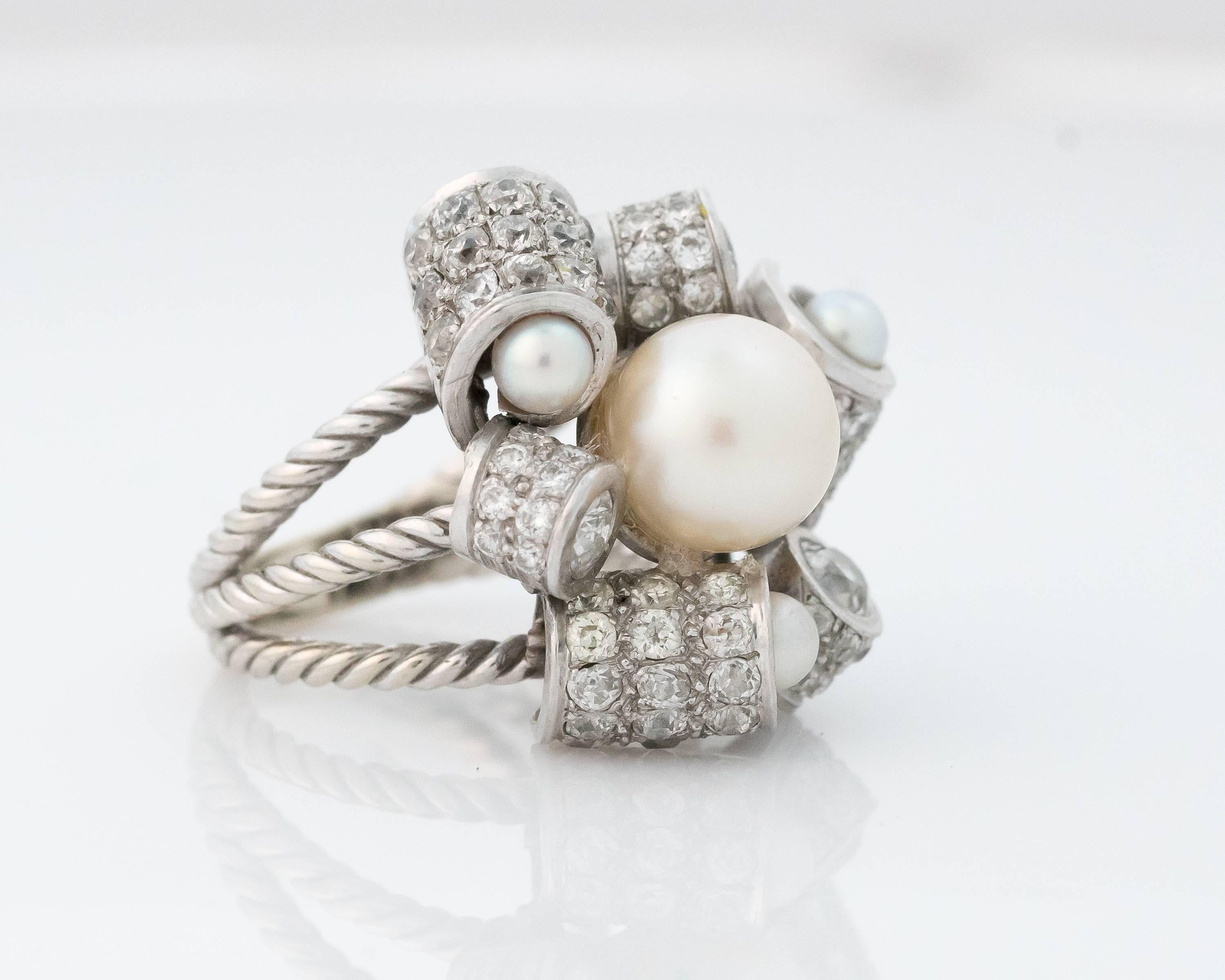 This gorgeous 1950s Pearl and Diamond Cluster Ring will make a statement wherever you wear it! 

The large 9.5 millimeter center white pearl is encircled by 6 diamond encrusted scroll motif cylinders. Each of the 3 larger cylinders is capped with a