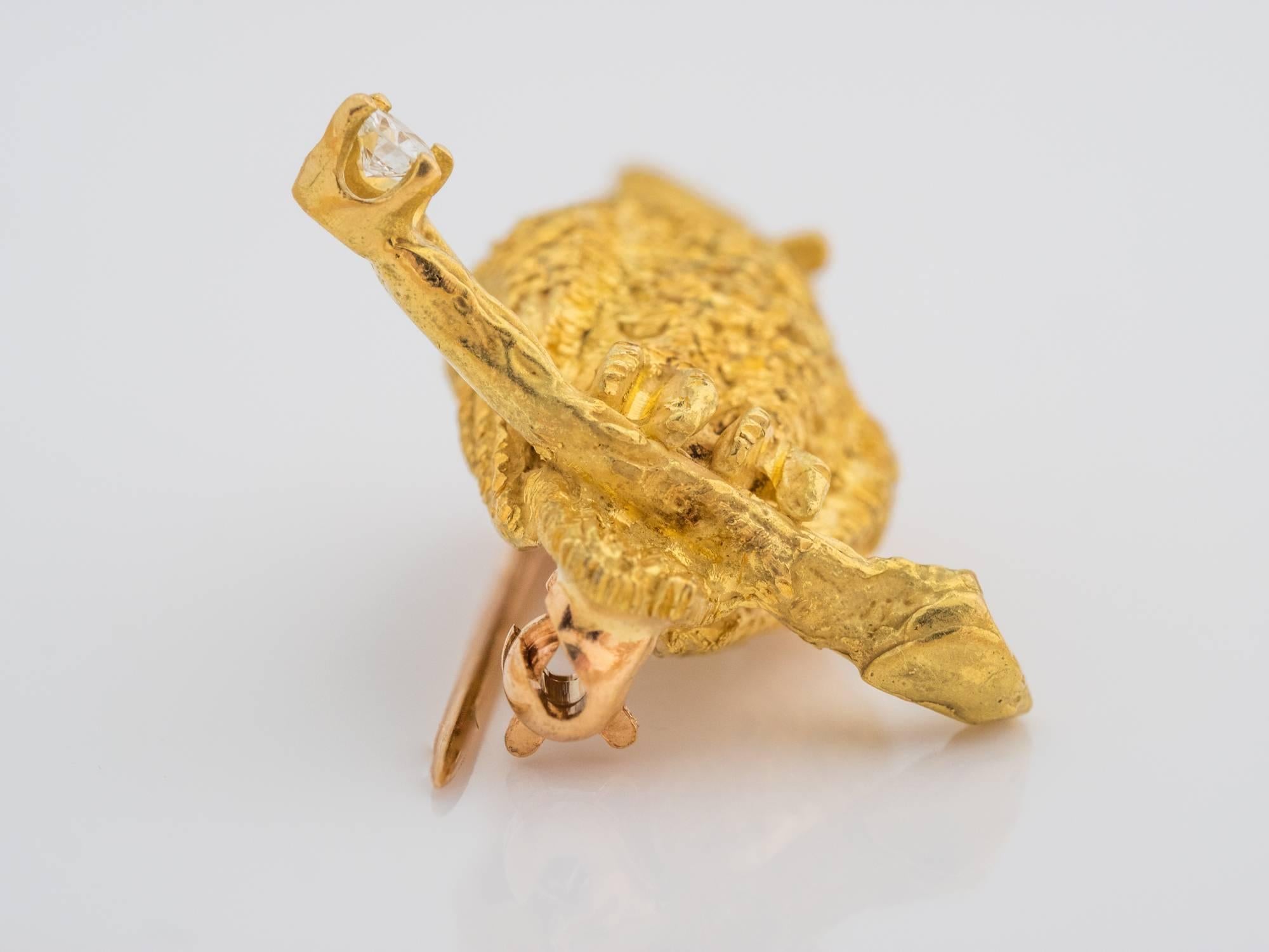 Unique owl pin crafted in solid 18k yellow gold. The owl has intricate hand-etched feather details throughout the body. It is perched on a twig, also made of 18k yellow gold, which is vertical to the bird. The bark on the twig has additional