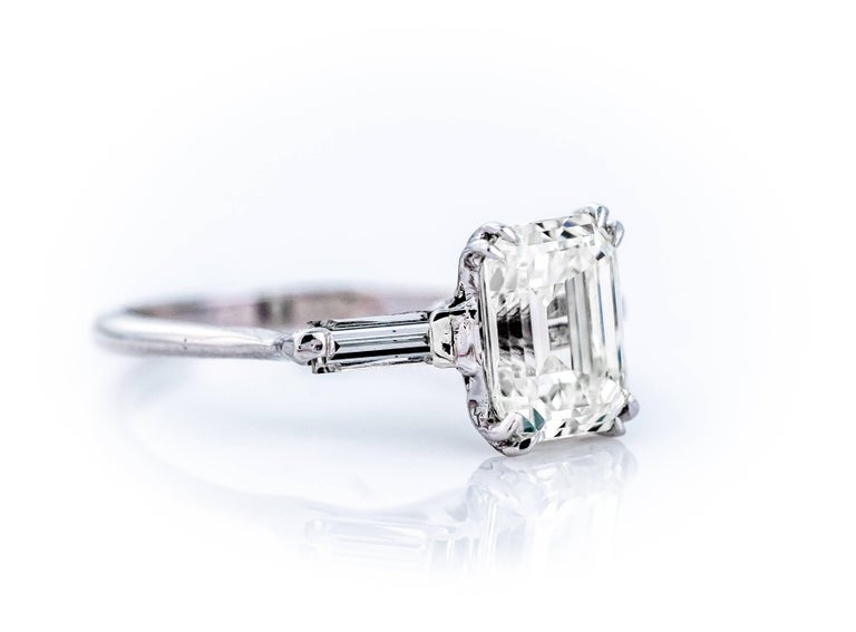 This GIA Certified 2.27 Carat Emerald Cut Diamond and 14 Karat White Gold Engagement ring features a center stone Double Prong Talon Set in each corner and flanked by 2 Baguette Diamonds weighing .10 carats each. This Vintage 1960s solitaire-style,