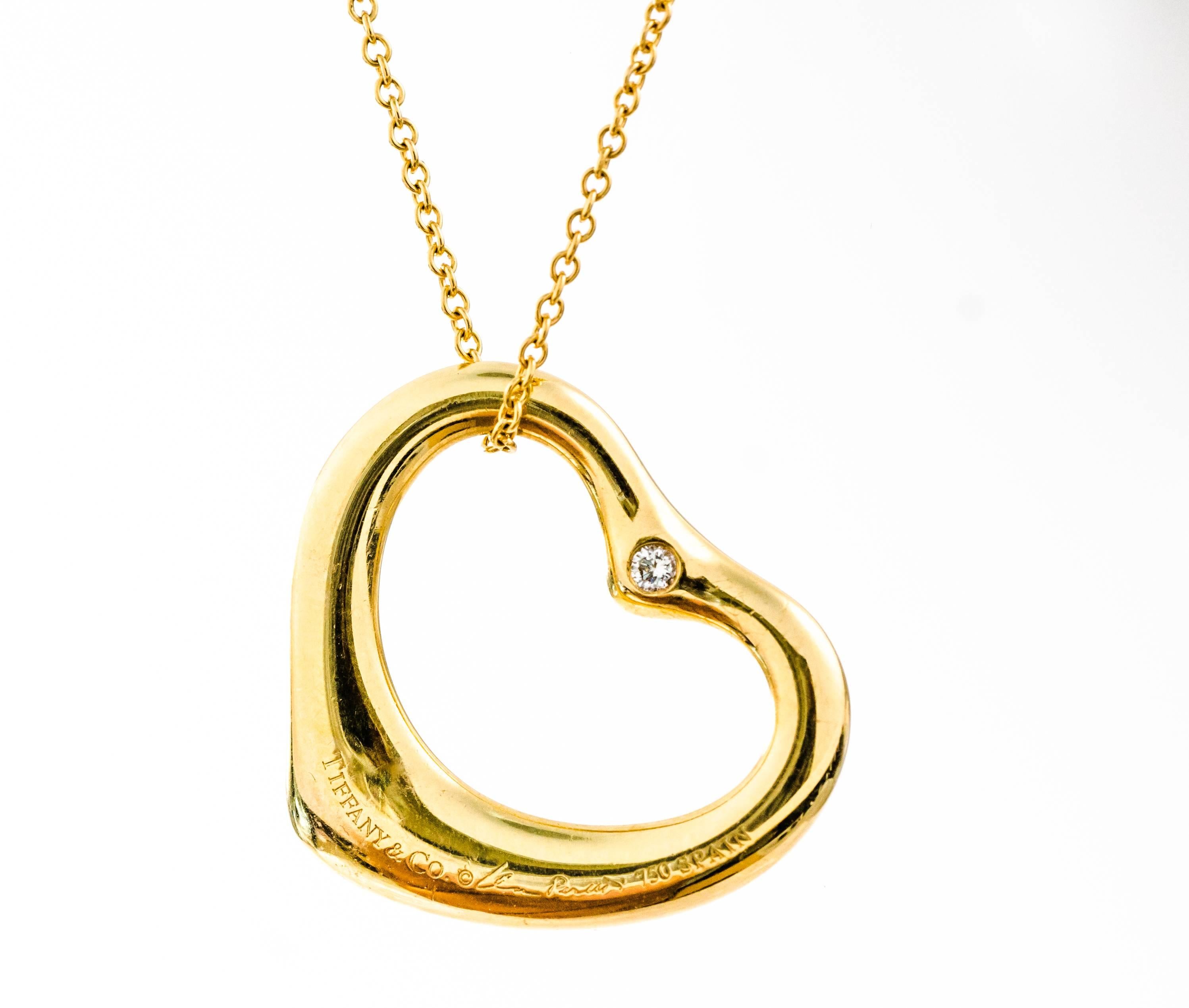 This 1990s Tiffany and Co. Diamond and 18K Yellow Gold necklace is from the Elsa Peretti Open Heart collection. This 15 inch long necklace features 6.7 grams of 18 karat yellow gold.  Two bezel set diamonds adorn the top of the heart pendant, one