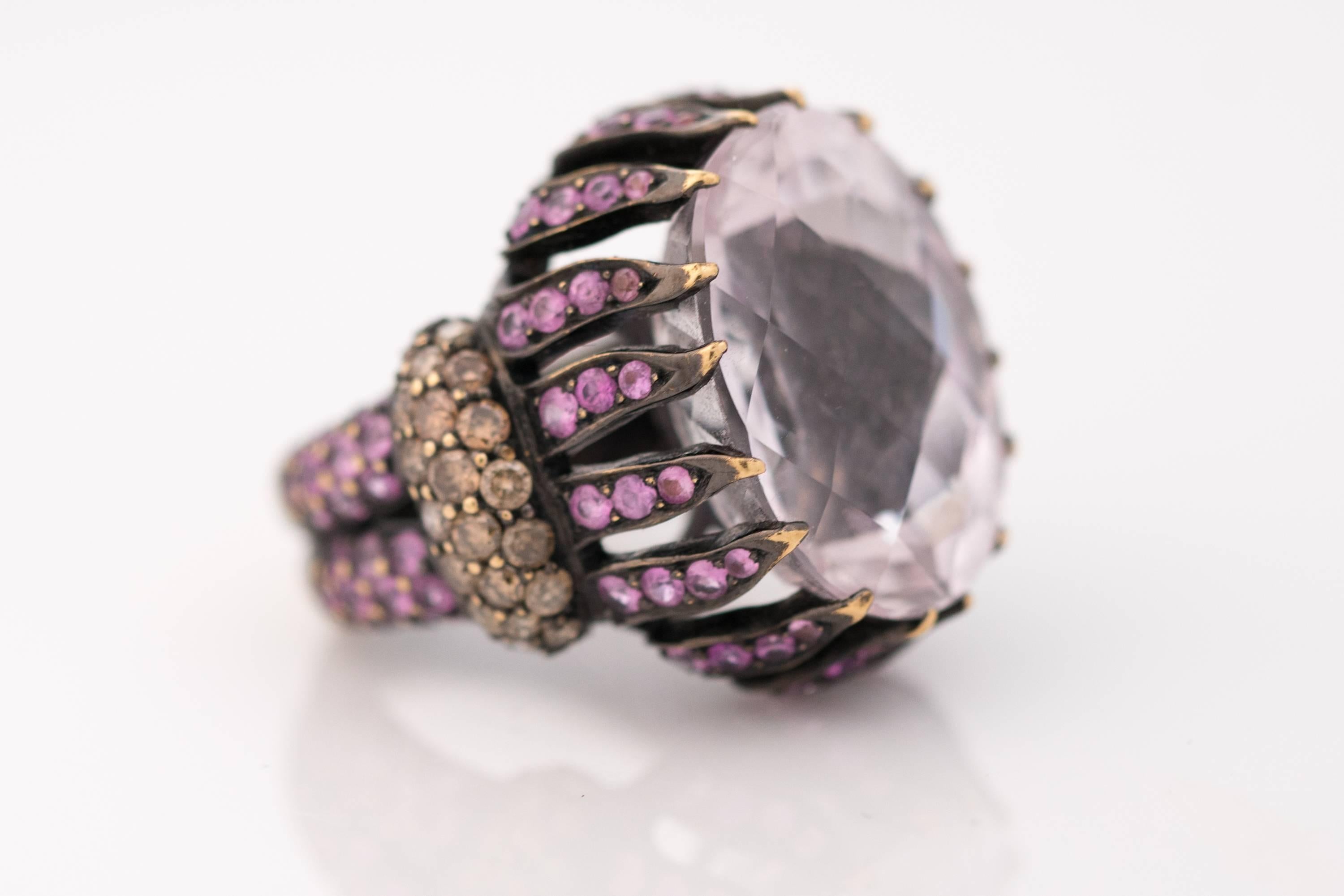 Wow! This 1990s ornate 15 Carat Pink Kunzite cocktail ring will make a statement at any occasion! The lovely Pink Kunzite center stone is surrounded by pink sapphires and natural champagne diamonds. This regal ring is crafted from 18 Karat Yellow