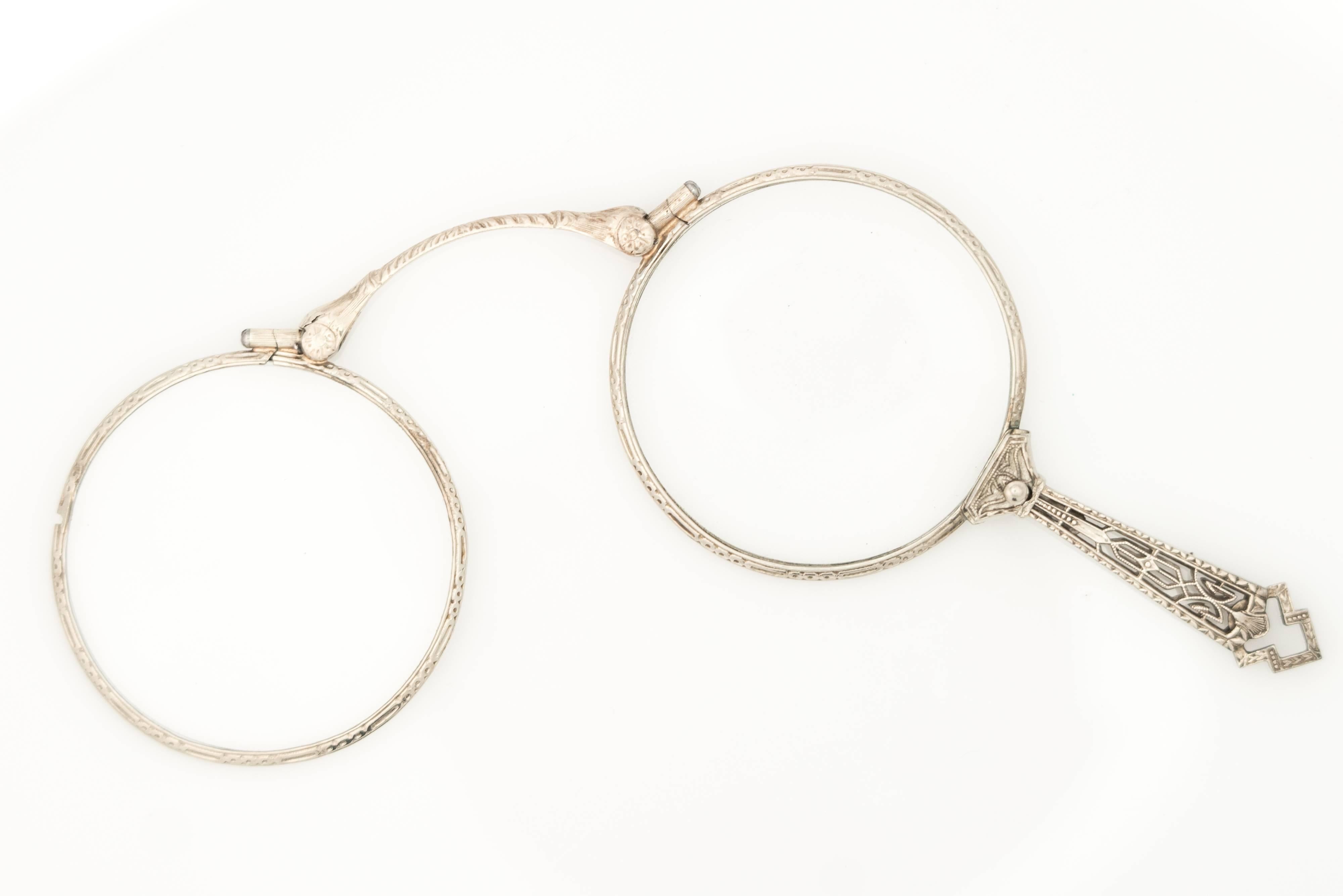 Diese atemberaubende faltbare 14 Karat Weißgold Lorgnette Brille aus den 1920er Jahren verfügt über 2 Gläser, die sich übereinander falten und einrasten lassen, um ein Vergrößerungsglas zu bilden. Ein kleiner Zughebel am oberen Ende des Griffs gibt