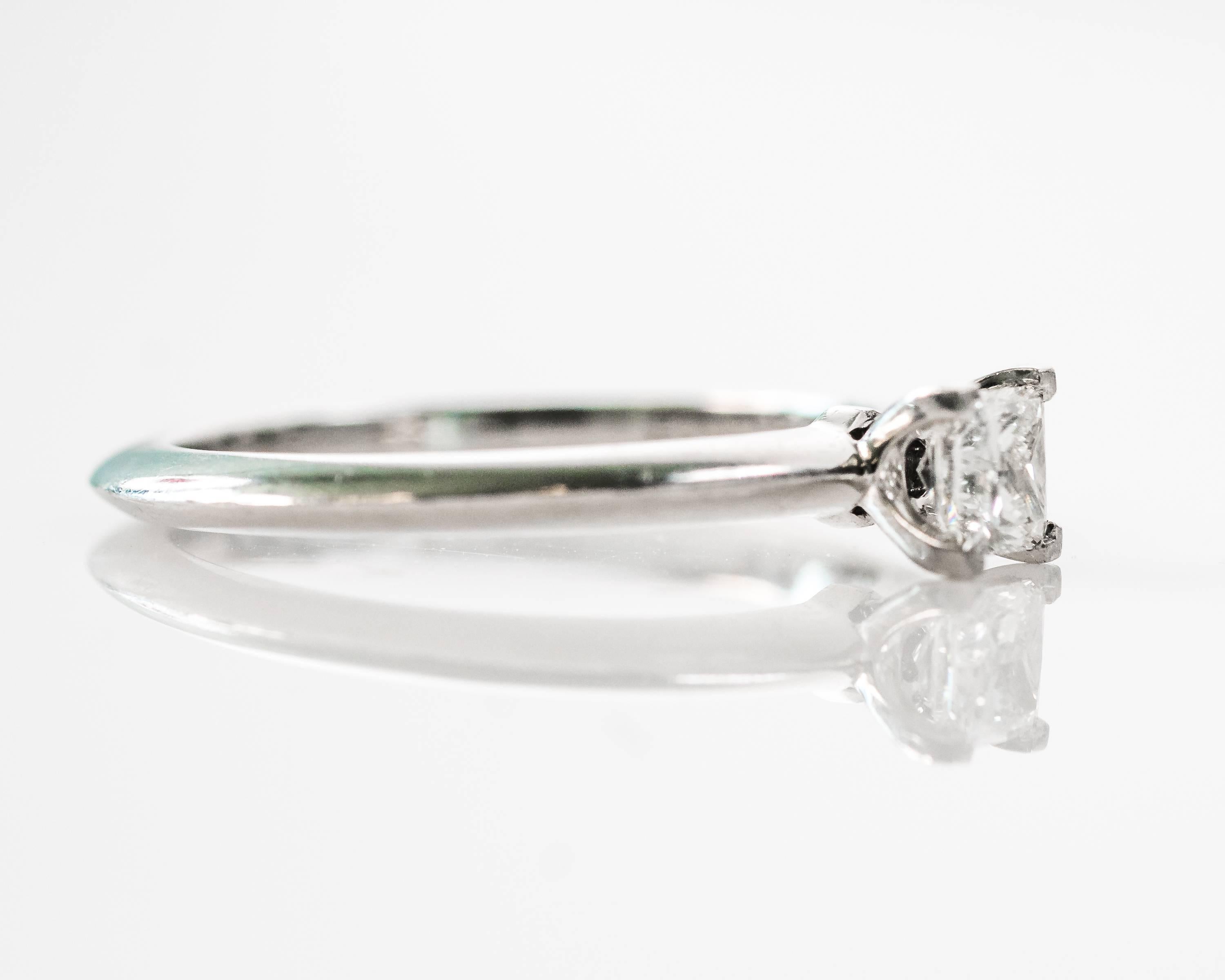 This Tiffany and Co. 0.33 carat Princess cut Diamond solitaire Engagement Ring features an F color, VS clarity diamond that sits flush in a four prong setting. 

Featuring a knife-edge Platinum band, this sweet ring comes with the original Tiffany