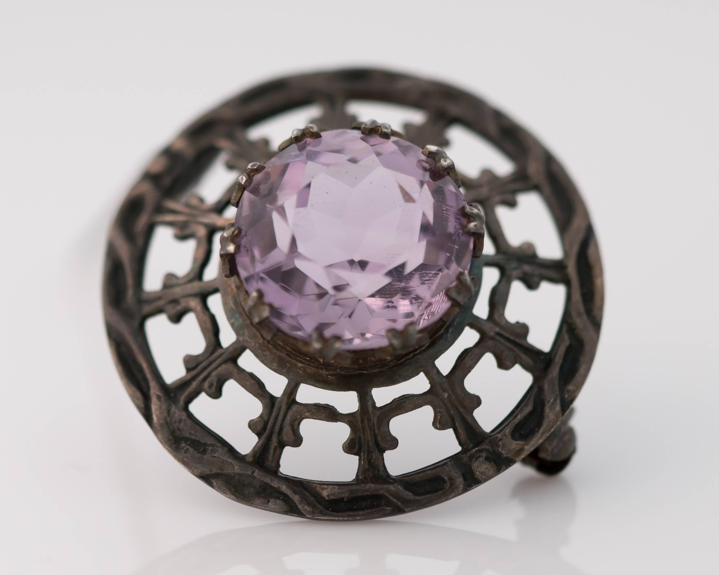 This 1910s Edwardian Era Brooch boasts a 10 Carat Old Miner Cut Amethyst set in Sterling Silver. This stunning 15 millimeter Amethyst is set with 10 talon double prongs for extra security. The classically patterned sterling silver has achieved a