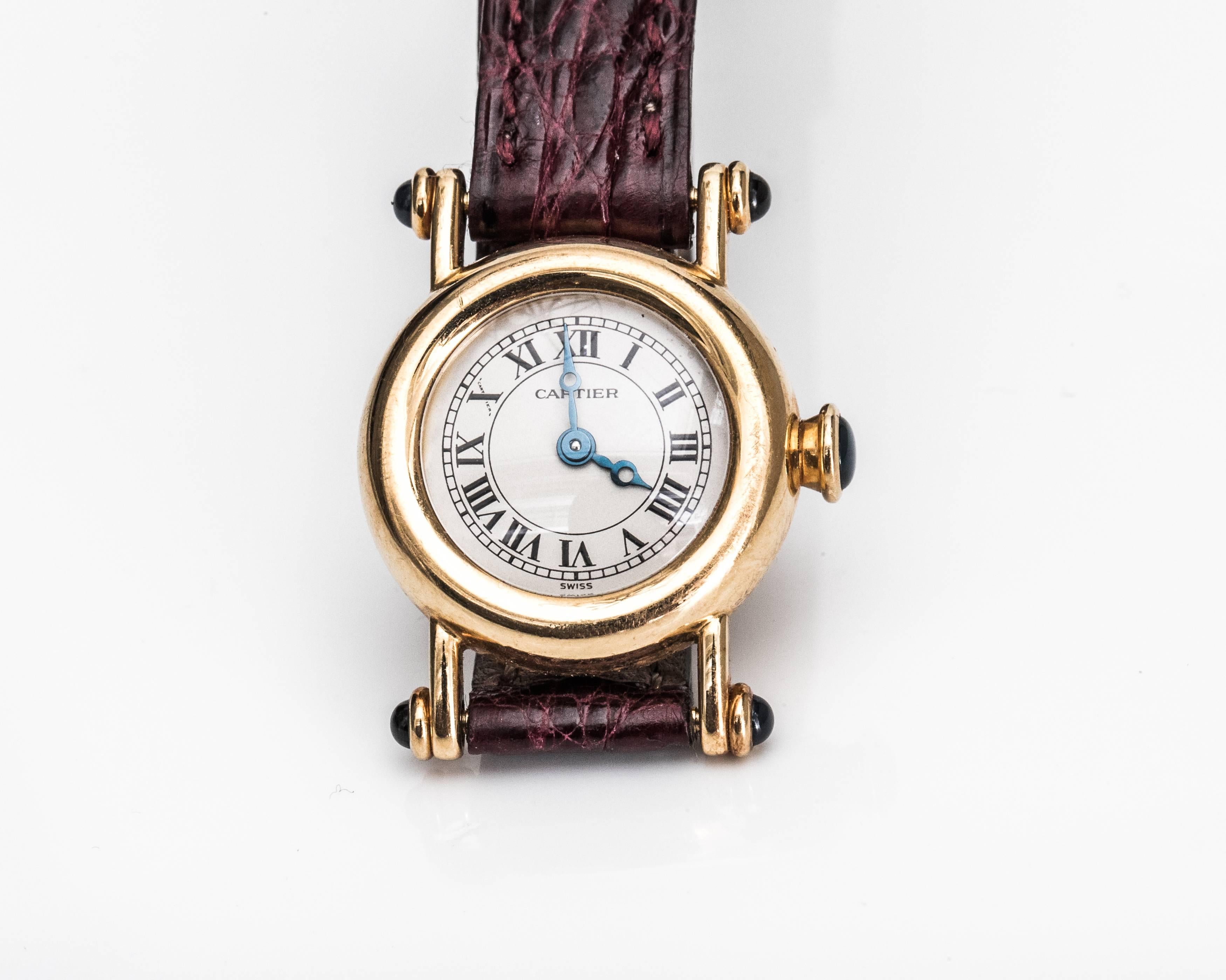 This gorgeous 1980s Swiss Made watch is a Cartier French classic. It features an 18 Karat Yellow Gold Case and clasp, 5 Sapphire Cabochons, white dial with black Roman Numeral Hour Markers, black Cathedral Hands and Quartz movement. The exquisite 18