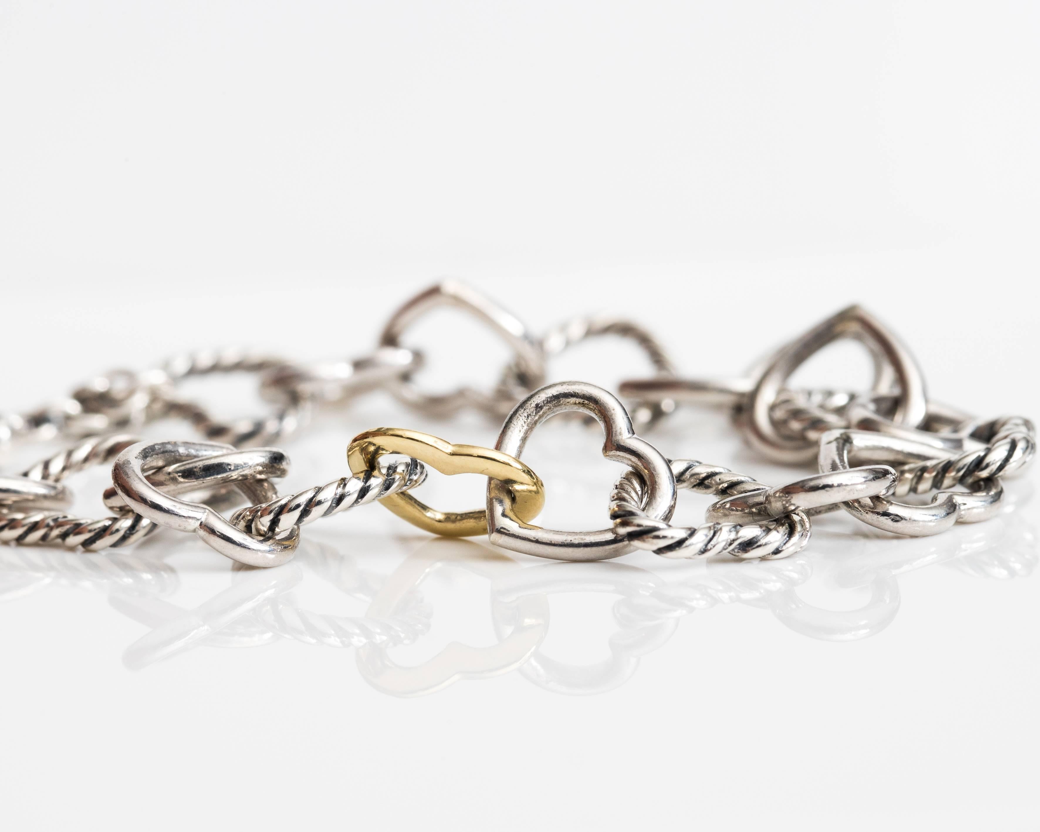 This David Yurman Heart Link Bracelet is a true Classic. Crafted from Sterling Silver and 18 Karat Yellow Gold, this bracelet features a Toggle Clasp and Interlocking Hearts. A single Sterling Silver Cable Heart links with 2 Smooth Silver Heart