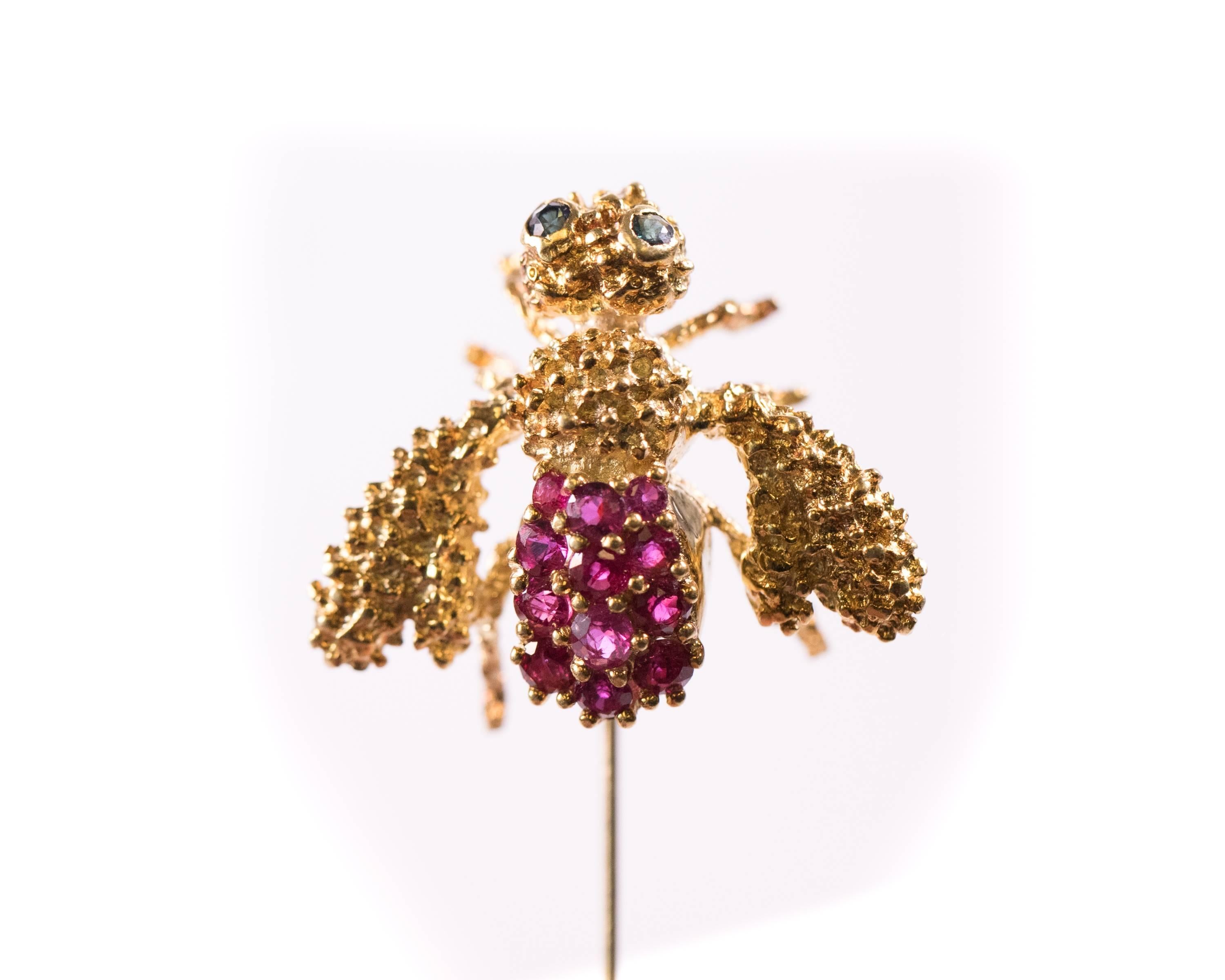 This vintage 1980s Ruby and Sapphire Bee Stick Pin is crafted from 18 karat Yellow Gold. It features 2 Blue Sapphire Eyes and a Ruby abdomen. The gold is heavily textured on the head, thorax, wings and legs. The gold underside of the bee is smooth.