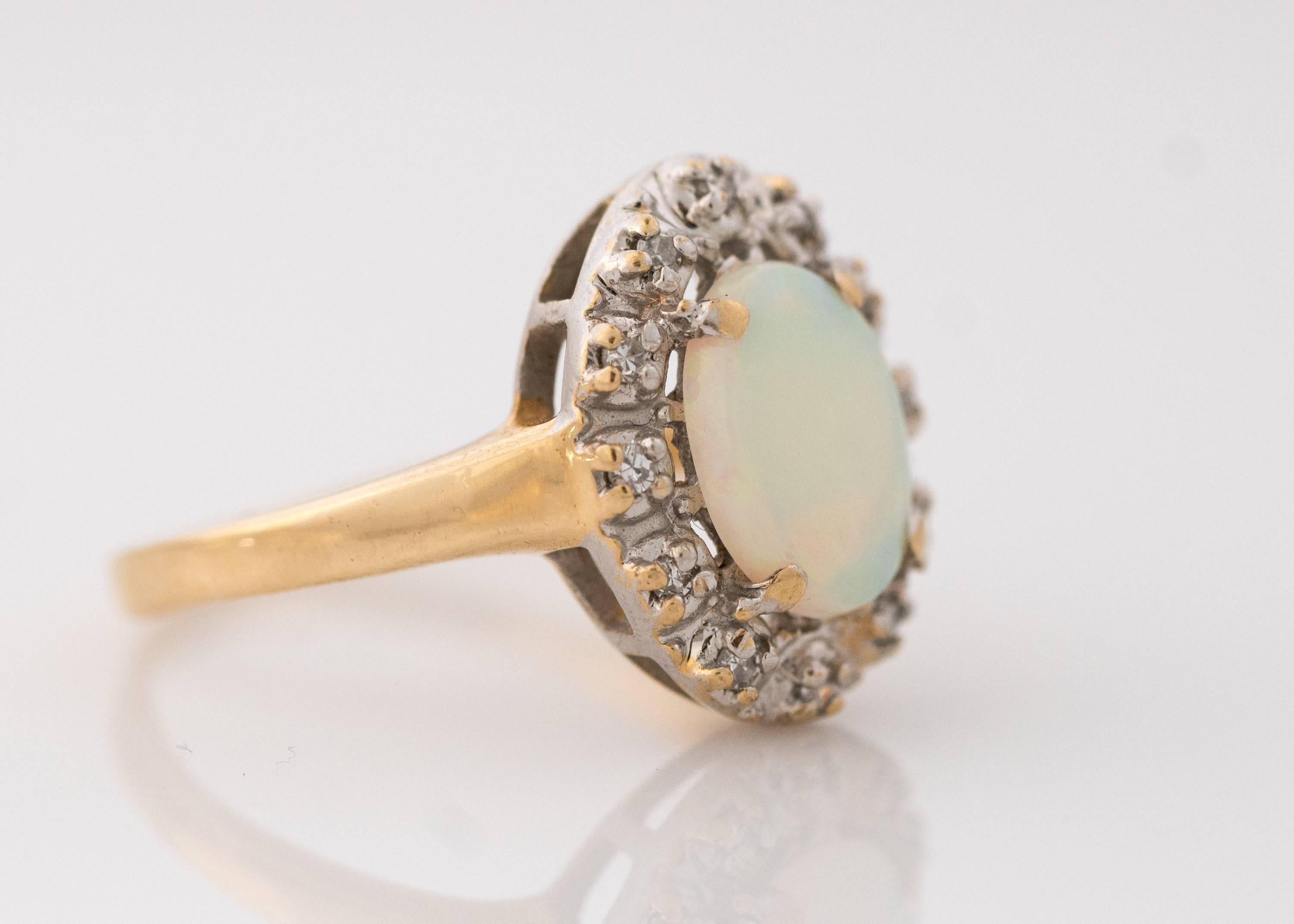 1960s Retro Opal with Diamond Halo, 14 Karat Yellow Gold Ring. Features a Natural Opal Cabochon with green and orange color play. The prong set Oval Opal measures 9 millimeters long by 7.1 millimeters wide. It is surrounded by a 0.10 carat total
