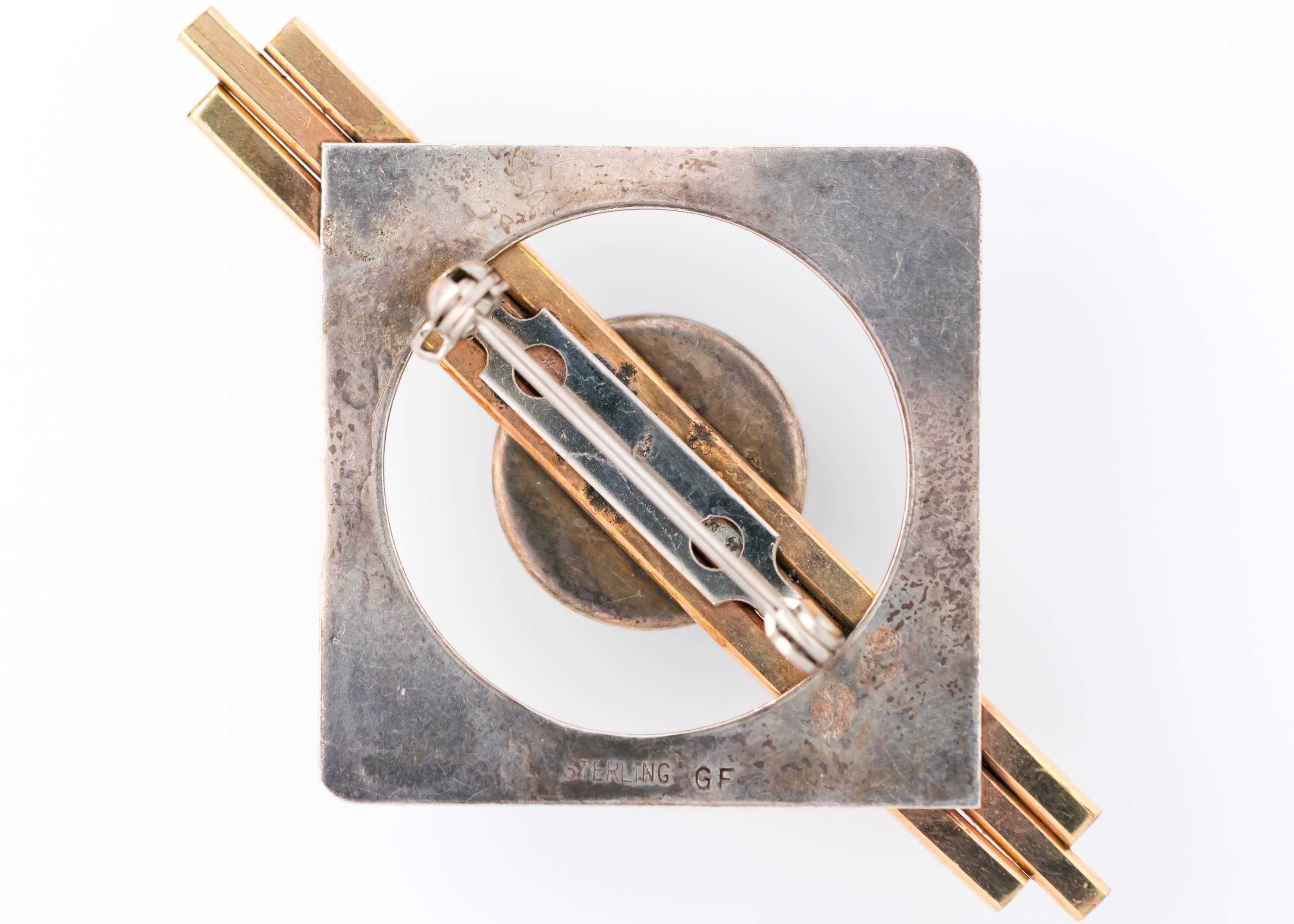 1950s Retro, Art Deco-Inspired Geometric Brooch. Features a Malachite Cabachon, 18K Yellow Gold Fill and Sterling Silver. The 14.5 millimeter Round Malachite cabochon is centered atop 3 parallel, horizontal gold bars. A Sterling Silver Square with a