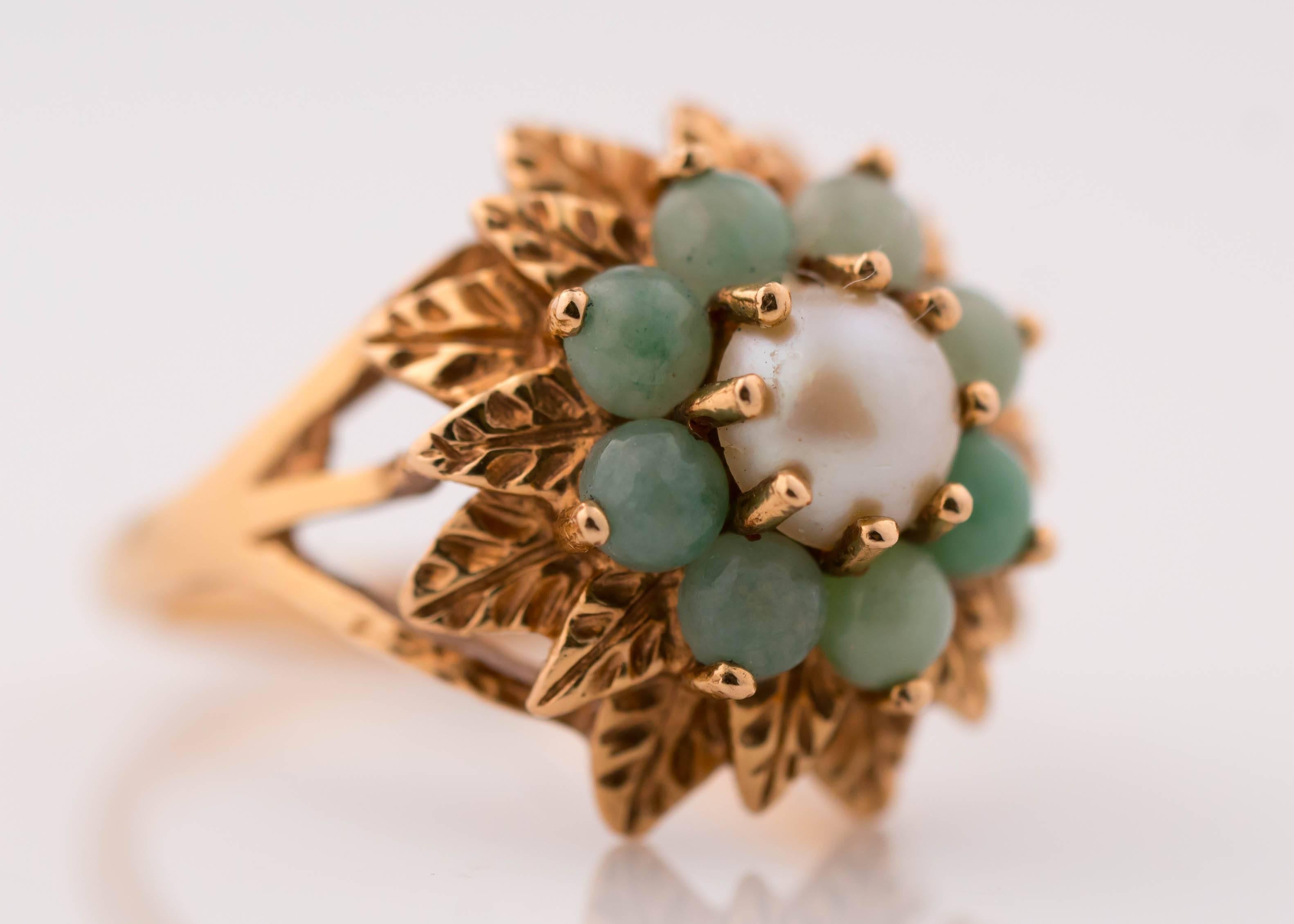 1950s Floral Ring - Jade, Pearl and 14 Karat Yellow Gold

Features a Pearl center encircled by 8 Jade cabochons. Behind the Jade are two rows of Gold Leaves set in 2 layers. The leaves are set at alternating heights, creating an illusion of fullness