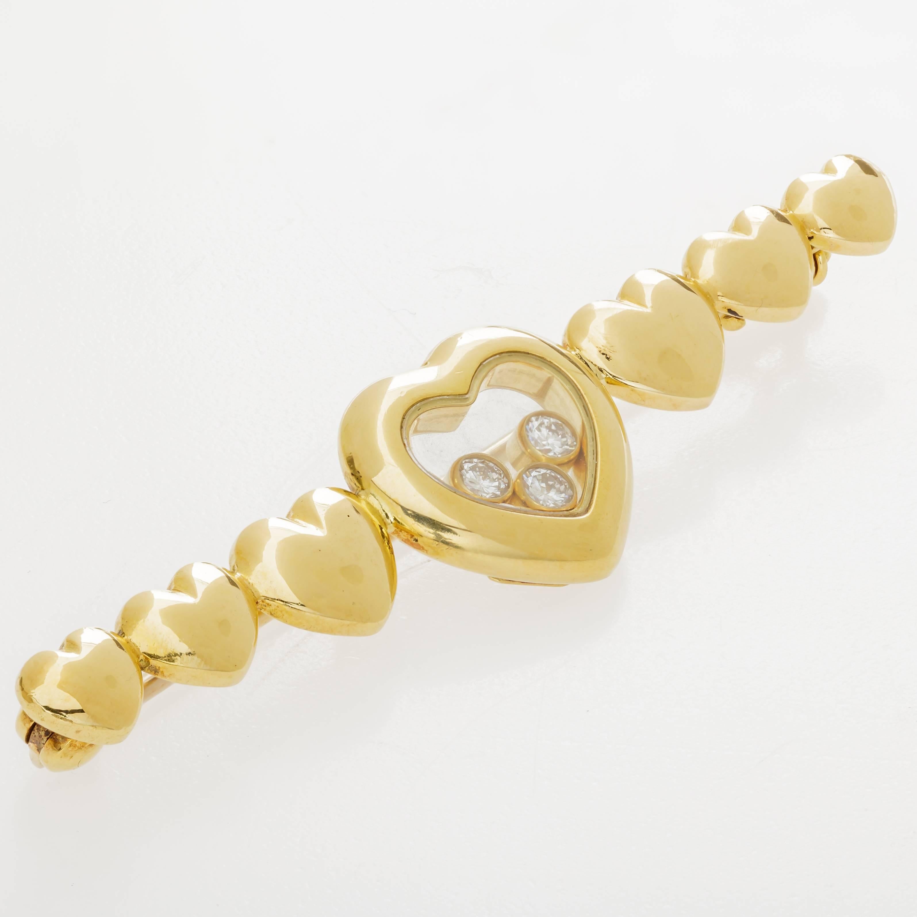 This Chopard Happy Diamonds pin features a design of seven hearts in 18K yellow gold, with the middle heart containing 3 floating diamonds totaling 0.17 ct.  The pin measures 2