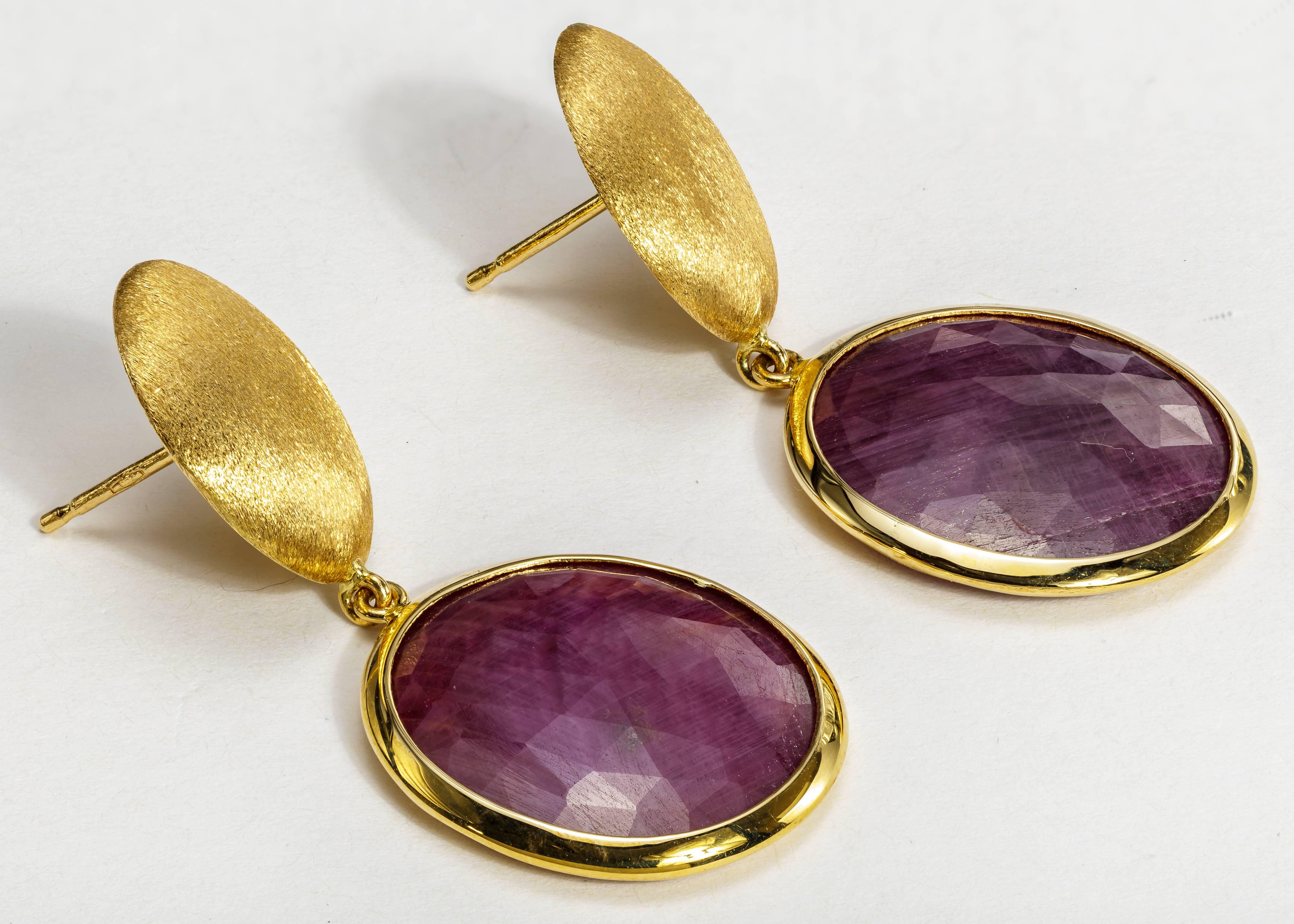 This pair of Yvel earrings features reddish purple sapphires set in satin brushed 18k yellow gold.