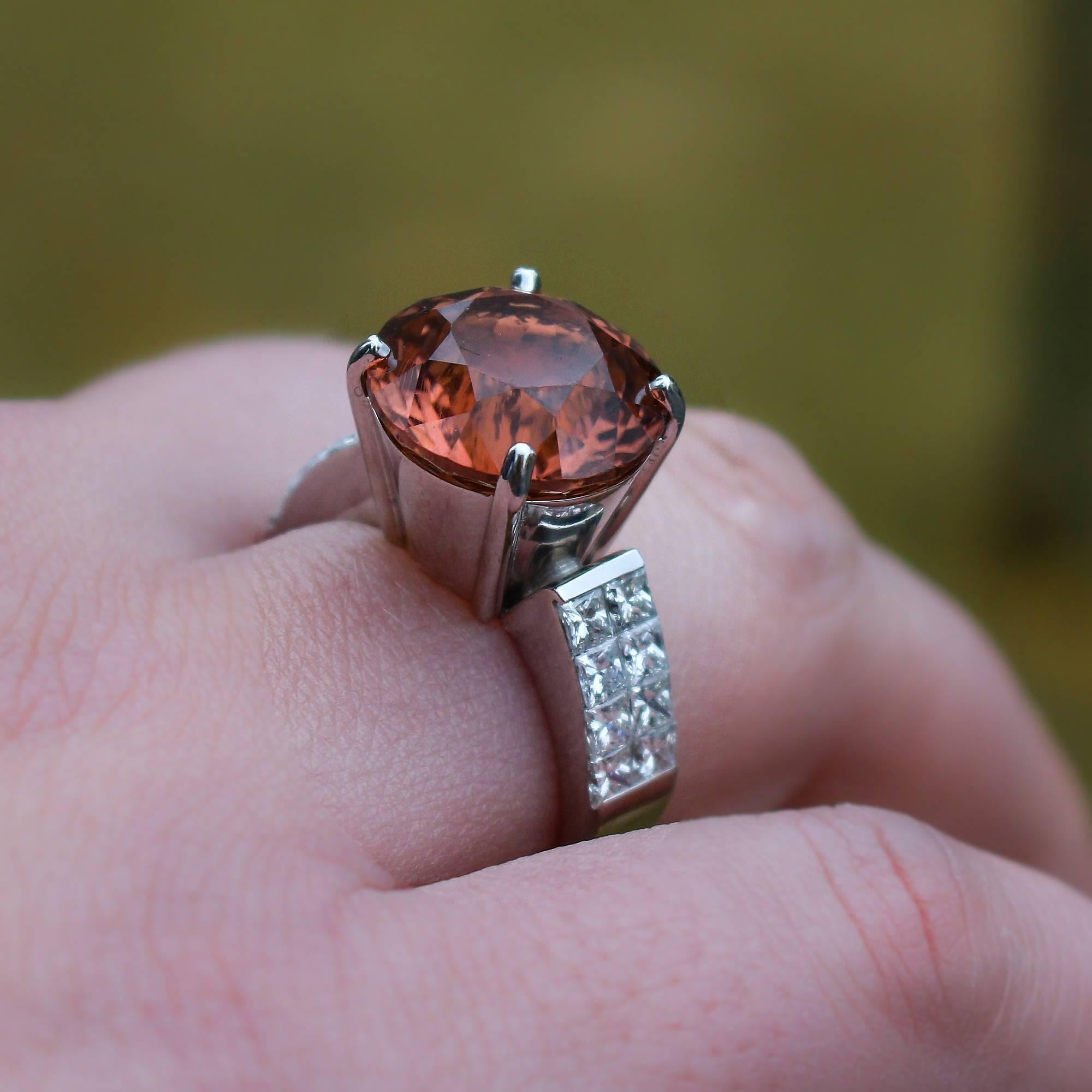 This fabulous ring centers a round tourmaline that weighs approximately 7.15ct and displays a beautifully unique strong pinkish orange color. It is set in a 18k white gold and diamond setting with 16 princess cut diamonds, which weigh approximately
