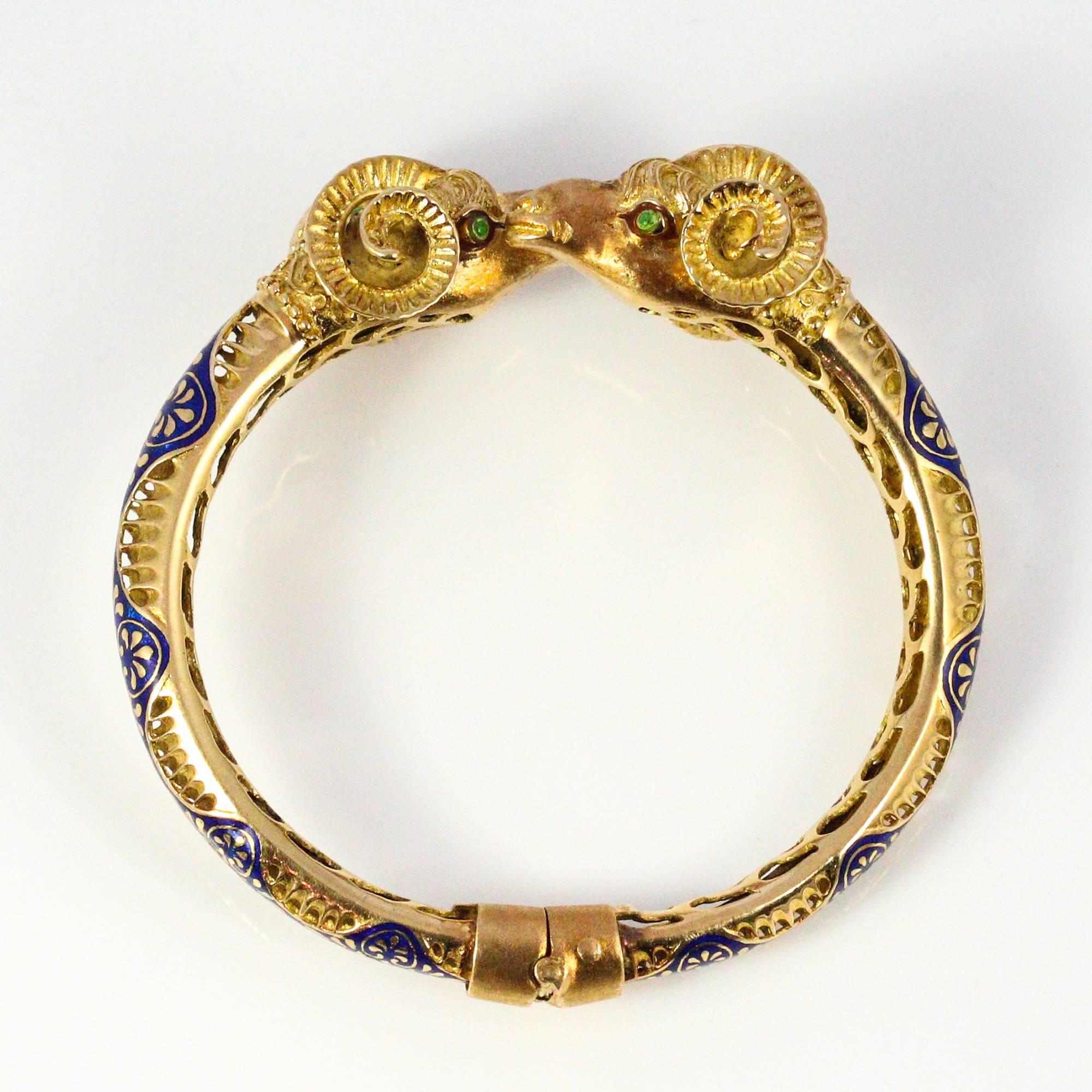 This fabulous, Modernist bracelet is made in 18k yellow gold with the focus being on two ram's heads that join in the center. The ram's heads are detailed with engraving and each accented with 3 cabochon emeralds at the top of their heads and 2