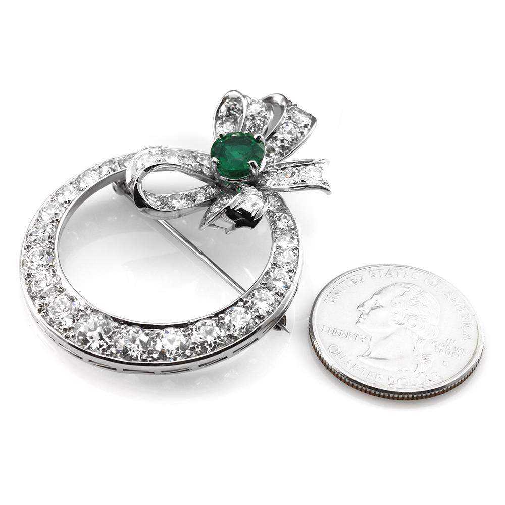 Pavé diamond and emerald bow wreath pin/ brooch in high polished platinum and 14K white gold. There is one round faceted emerald (1.88ct) and fifty-two European cut diamonds (10.41ctw) with a color of H-I and a clarity of VS-SI. The emerald is