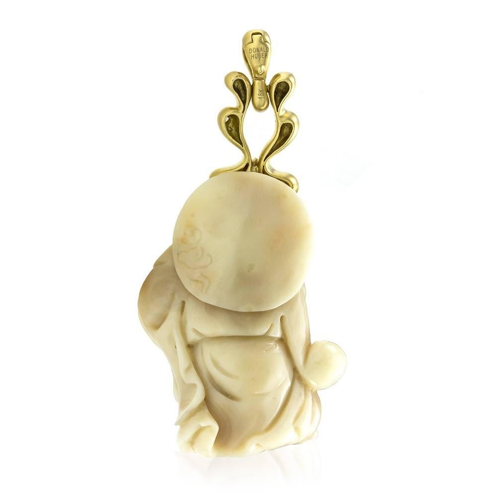 Donald Huber carved white coral Buddha with diamond accents pendant/ enhancer set in 18K yellow gold. There are one carved white coral (appx. 35.9mm x 26.5mm) and twenty-eight round brilliant cut diamonds (0.17ctw) with a color of F-H and a clarity