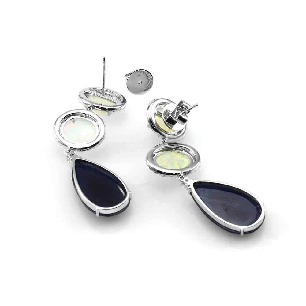 Opal, blue sapphire, and pavé diamond dangle earrings set in 18K white gold. There are two oval opal cabochons (7.64ctw), two pear shaped faceted sapphire slices (19.23ctw), and ninety-four round brilliant cut diamonds (1.28ctw) with a color of H-I
