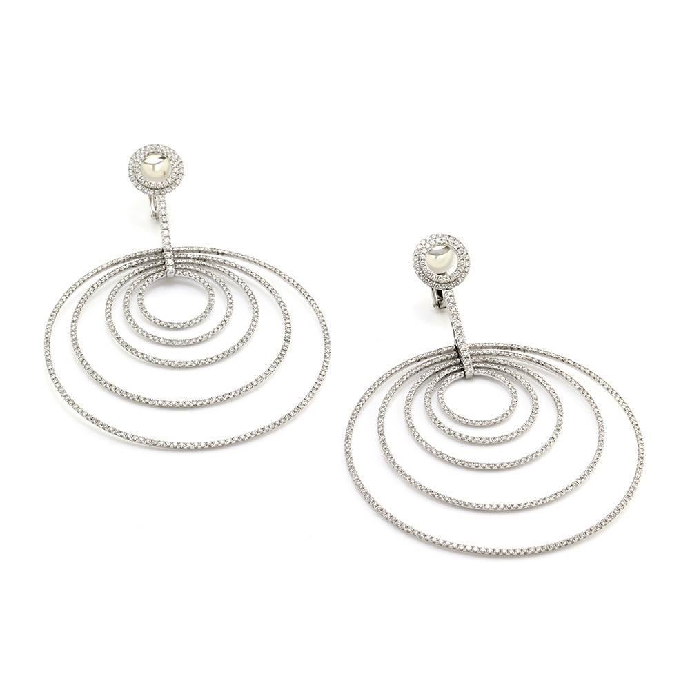 Pavé diamond open five circles in motion dangle earring set in 18K white gold. There are eight hundred eighty-eight round brilliant cut diamonds (7.36ctw) with a color of H-I and a clarity of VS. The diamonds are bead set in high polish gold. The