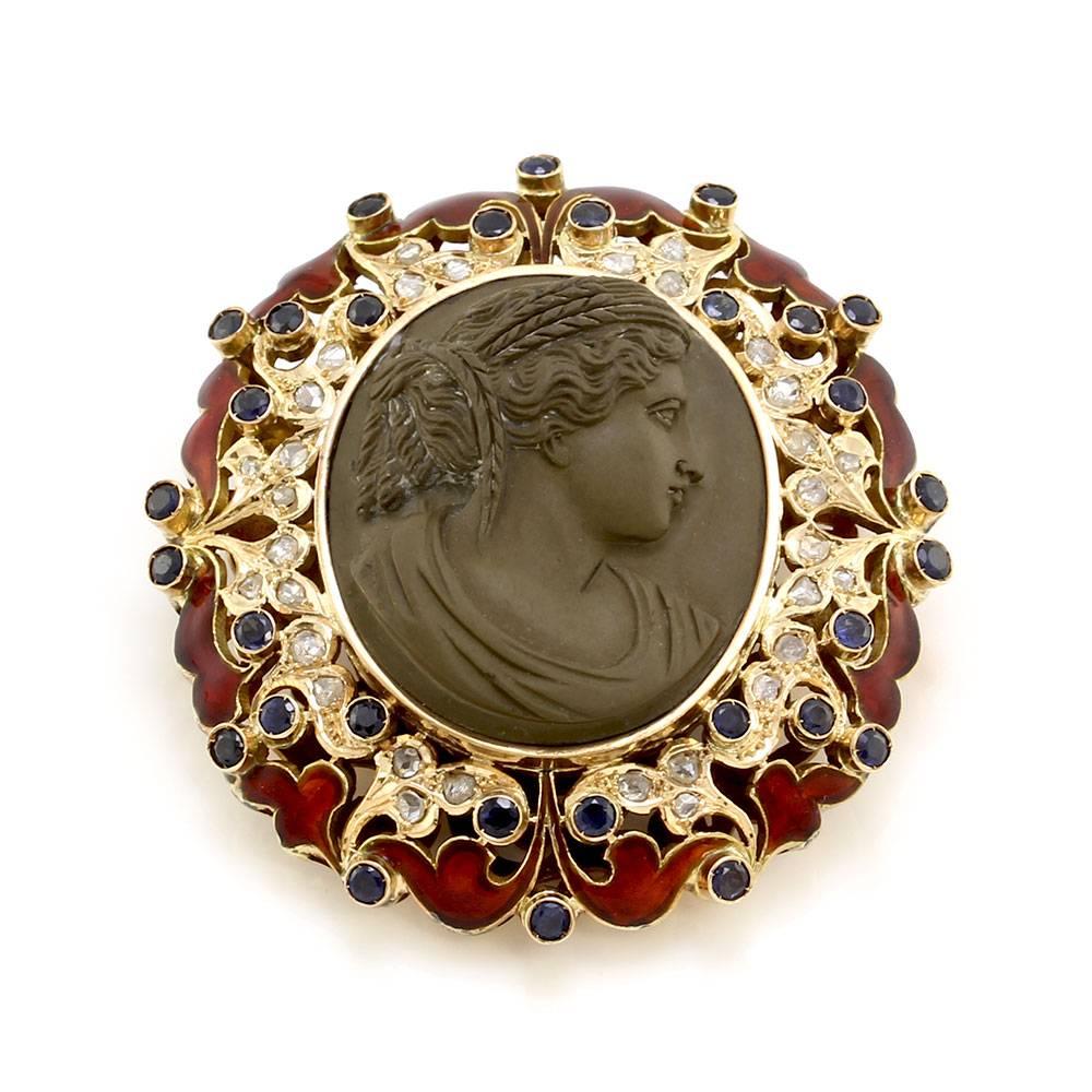 Charming lava cameo pendant brooch with blue sapphires, diamonds and red enamel set in 14K yellow gold. There are one carved lava cameo (31.2mm x 26.2mm), thirty round faceted sapphires (1.80ctw), and thirty-two rose cut diamonds (0.16ctw). The lava