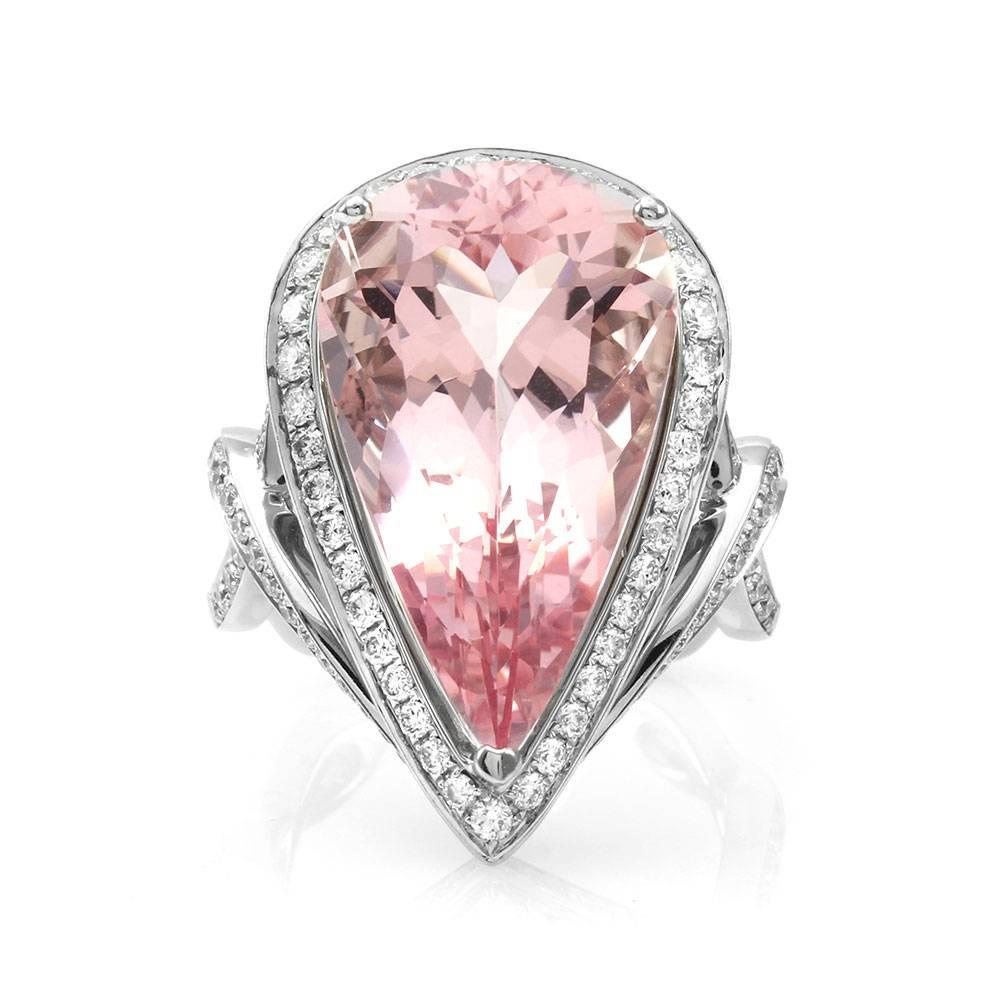 Morganite and pavé diamond halo ring in 18K white gold. There are one pear brilliant cut morganite (12.18ct) and one hundred seven round brilliant cut diamonds (1.06ctw) with a color of G-H and a clarity of VS. The morganite is prong set, and the