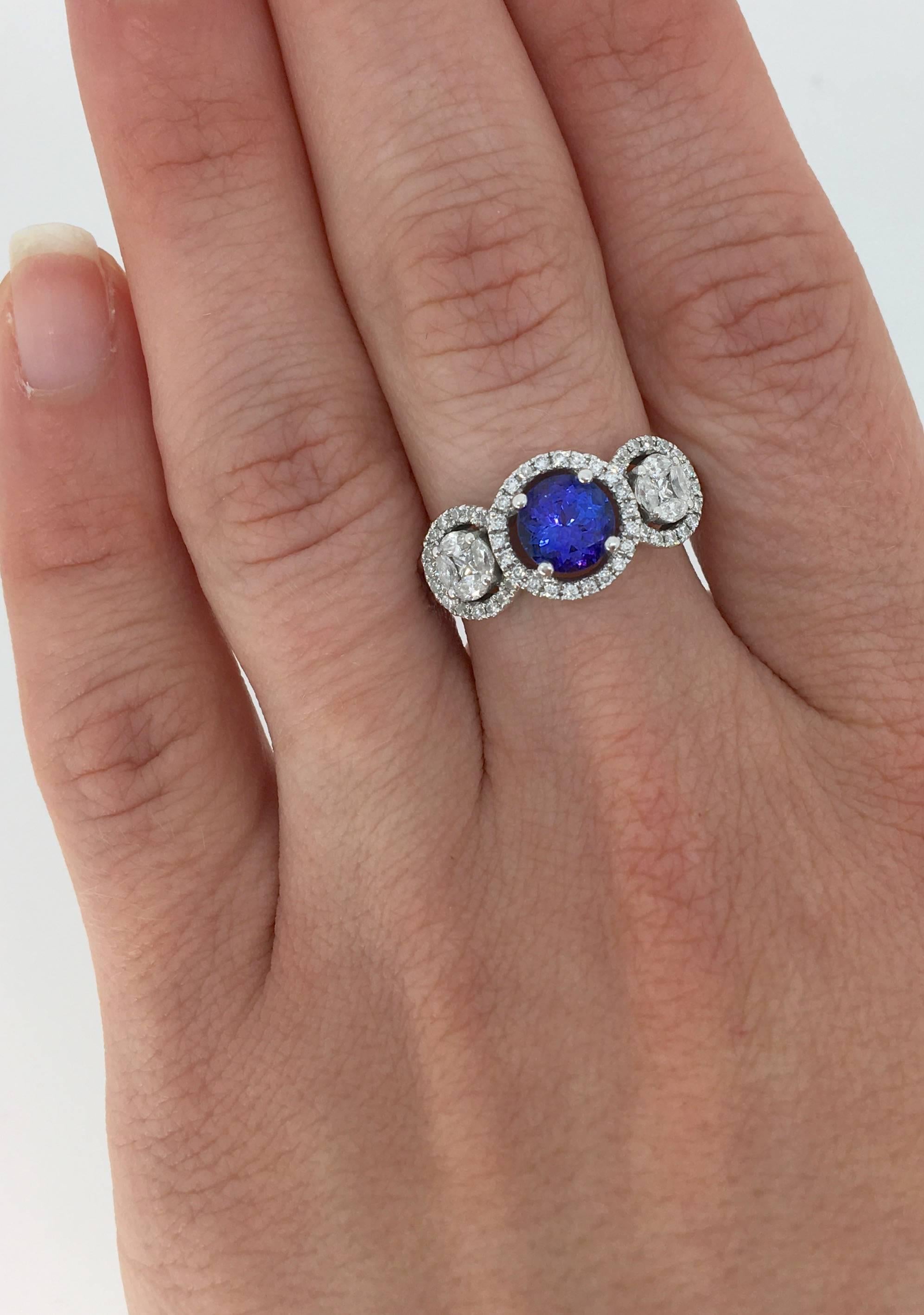 This timeless 14K White Gold Three stone halo Diamond and Tanzanite Ring Features a 6.4MM Round Tanzanite Stone.  The beautifully accented side stone halos contain two Princess cut Diamonds and 8 additional surrounding Marquise cut Diamonds. The