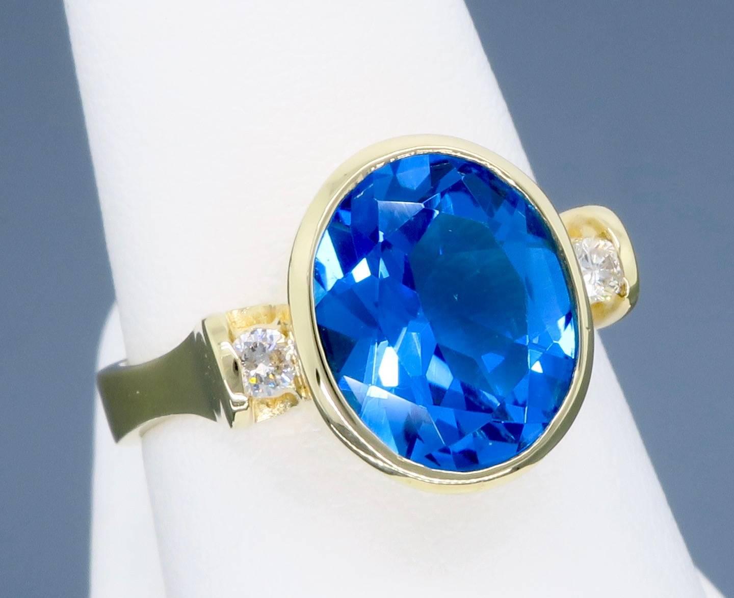 This gorgeous ring features a bezel set large oval cut blue topaz with deep blue color. The featured gemstone is approximately 10.58MM X 8.79 MM X 5.70MM, and is accented by two beautiful Round Brilliant Cut Diamonds. There is approximately .10CTW