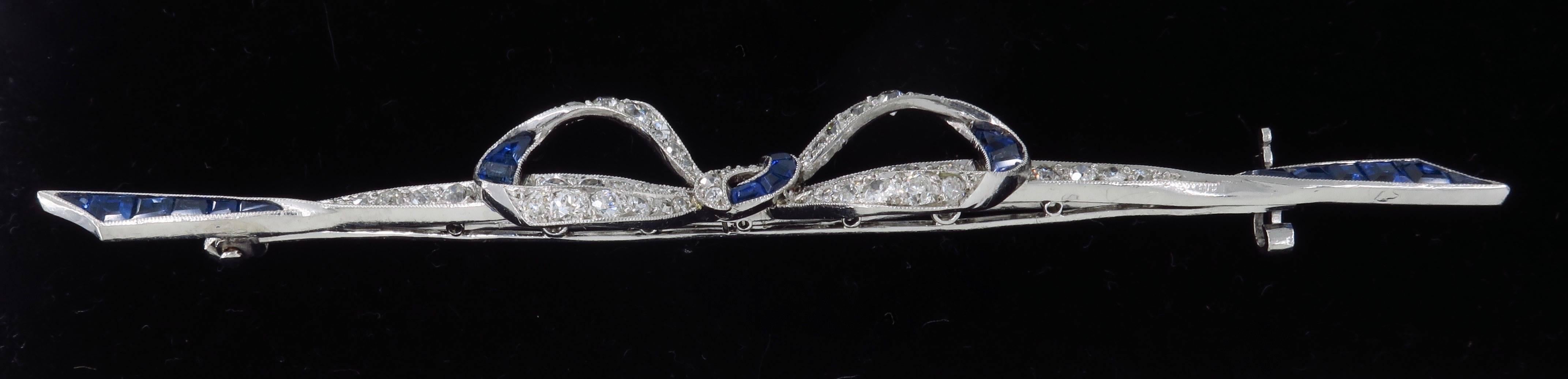 This stunning pin is elegantly adorned with Old European Cut Diamonds, Old Miner Cut Diamonds and Blue Sapphires. There is approximately 1.08CTW of diamonds in this unique bow designed pin. The diamonds display F-H color and VS2-I1 clarity.  The