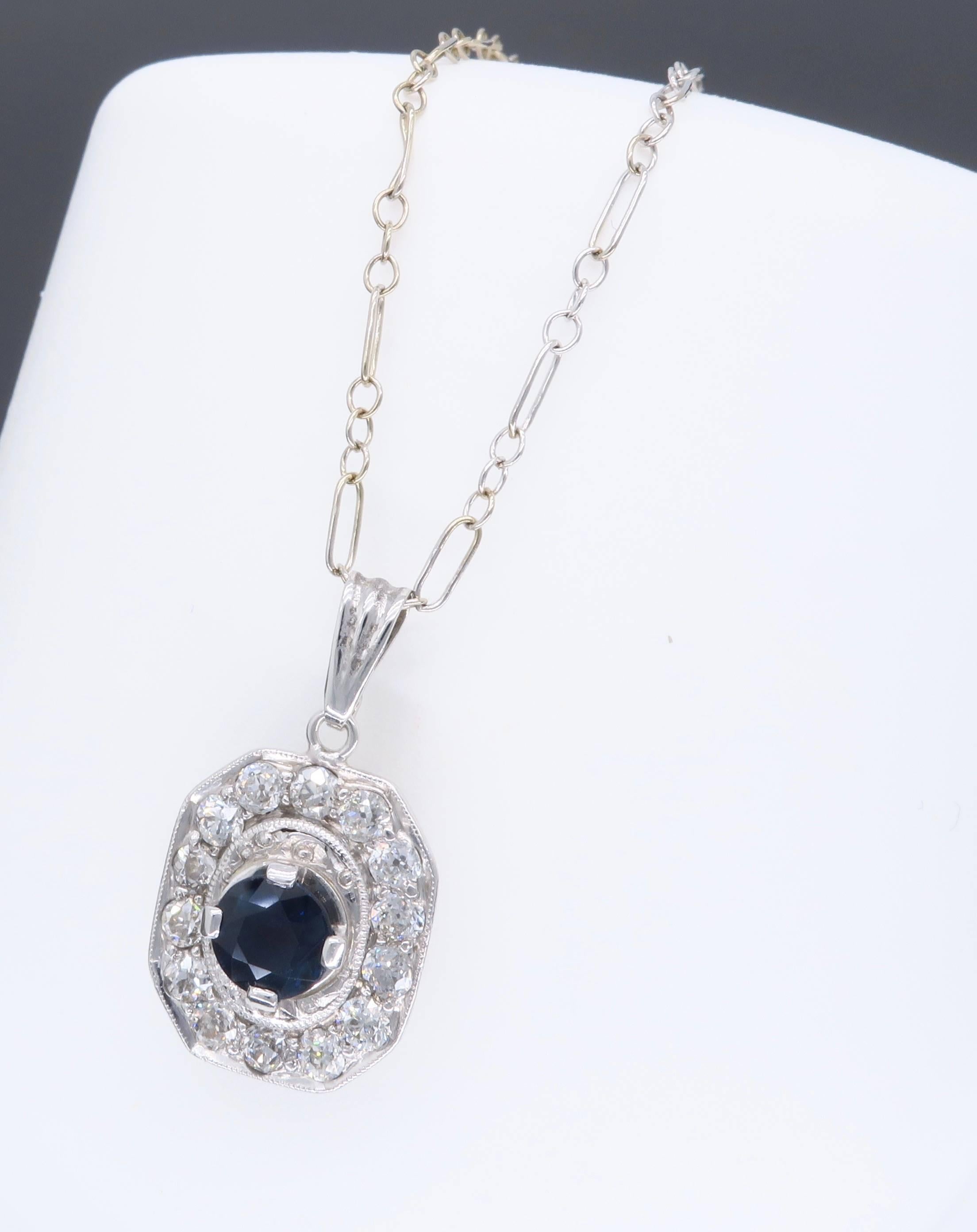 This Art Deco Platinum pendant features a dark blue 5.1MM Sapphire with 14 Old European Cut Diamonds surrounding it. There is approximately .55CTW of diamonds displaying an average color of F-H and average clarity of VS.  The 14K white gold chain is