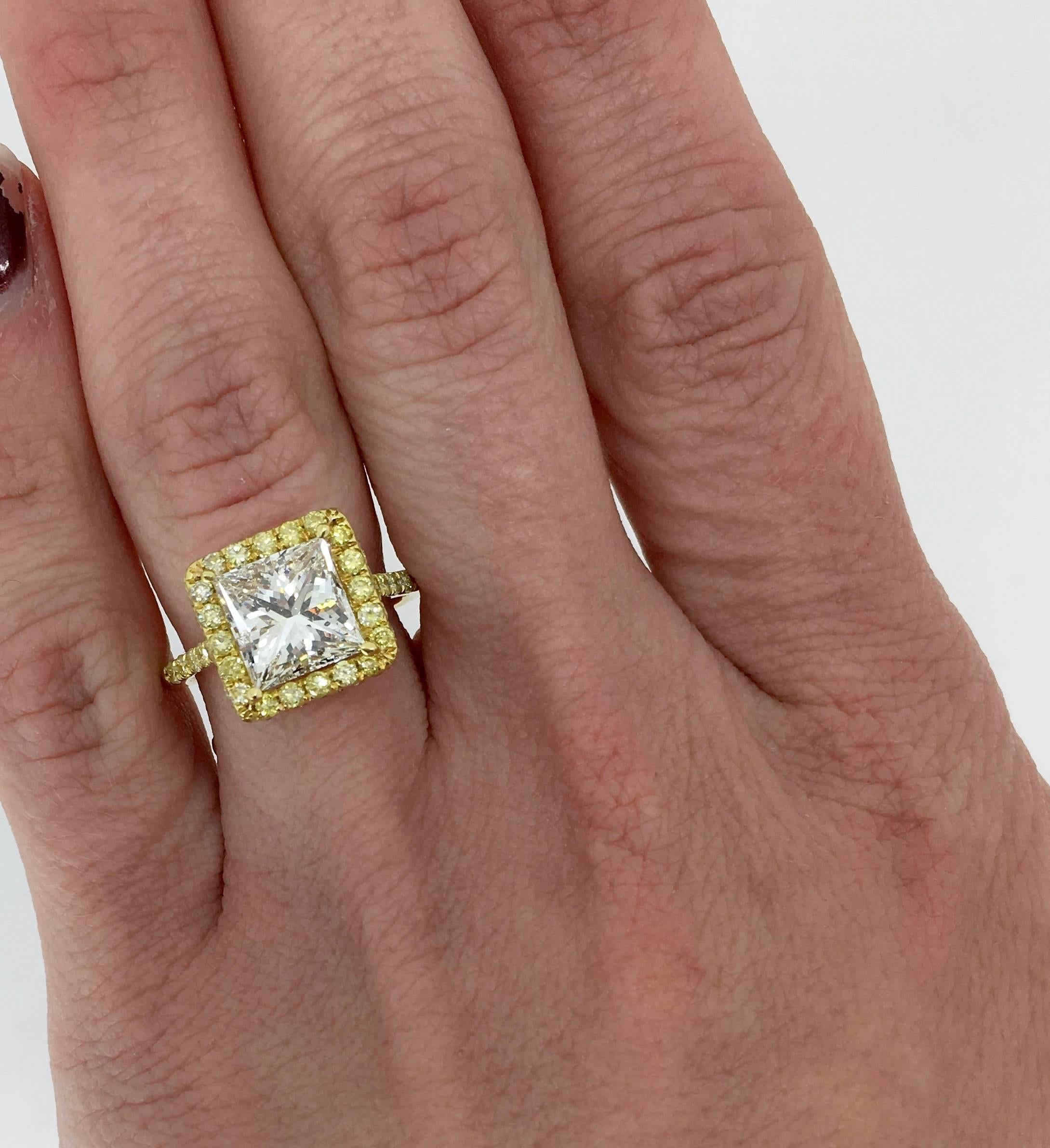 Stunning ring features an approximate 3.03CT Princess Cut Diamond in the center displaying J-K color and SI2 clarity. The 18K yellow gold ring is adorned with Yellow Round Brilliant Cut Diamonds all the way around the center stone and down the