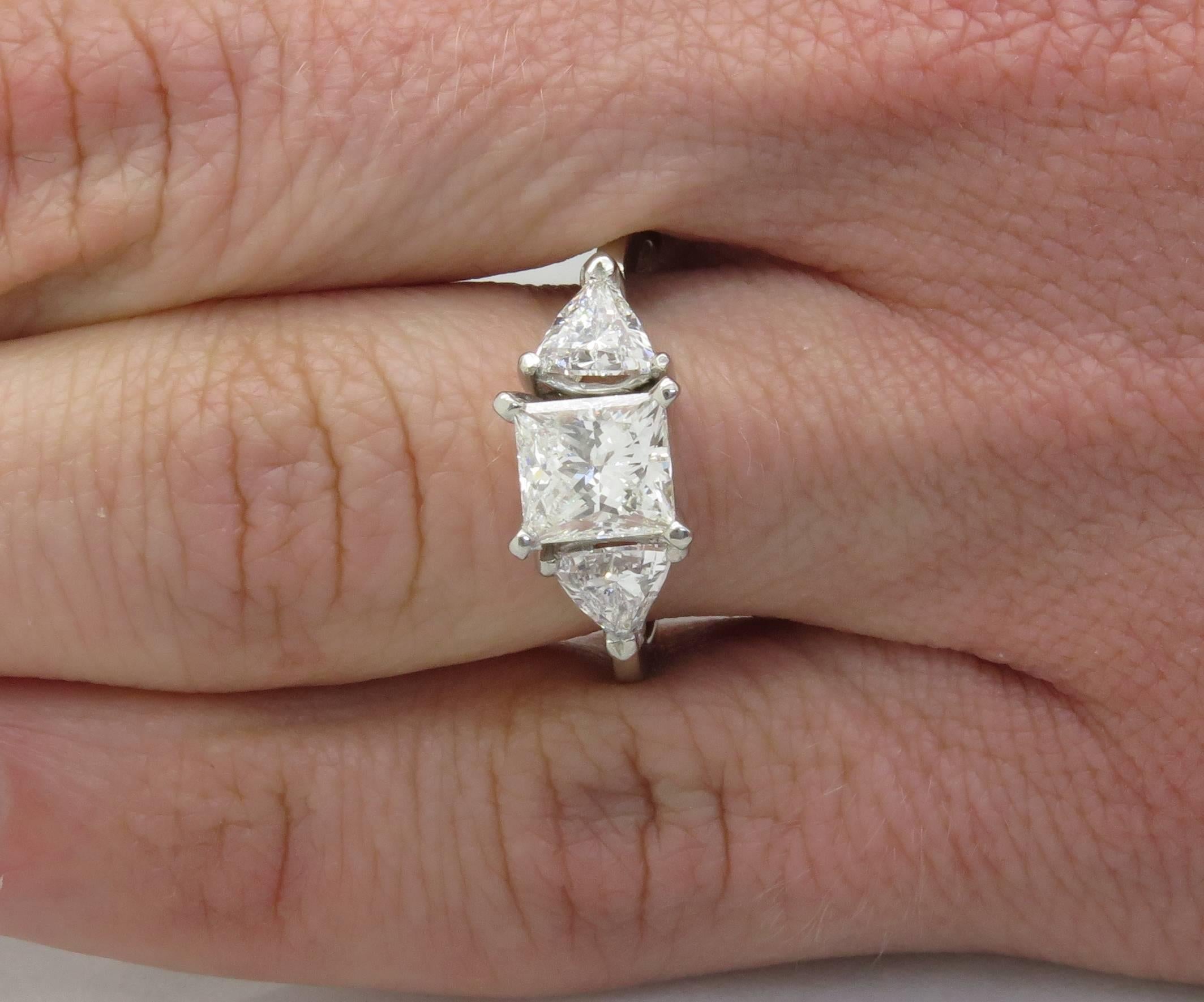 This platinum ring features a GIA Certified 1.23CT Princess Cut Diamond, with two Trilliant Cut Diamonds flanking it. The center diamond has G color and VS2 clarity. The total diamond weight is approximately 2.02CTW. The platinum ring is size 6.5