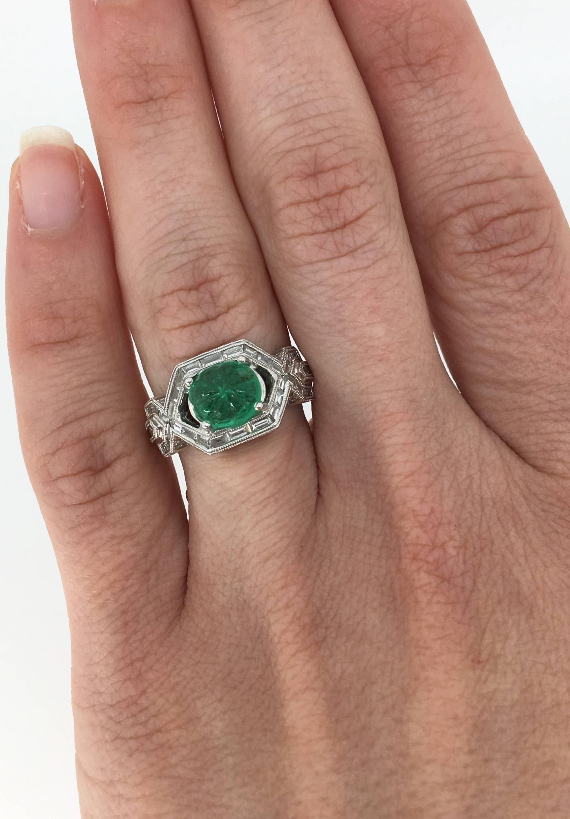 This unique ring features a beautiful 7.7MM X 6.8MM carved emerald in the center. The emerald is accented with 42 Baguette Cut Diamonds and 86 Round Brilliant Cut Diamonds set into a custom setting. The diamonds have G-I color and I-VS clarity. The