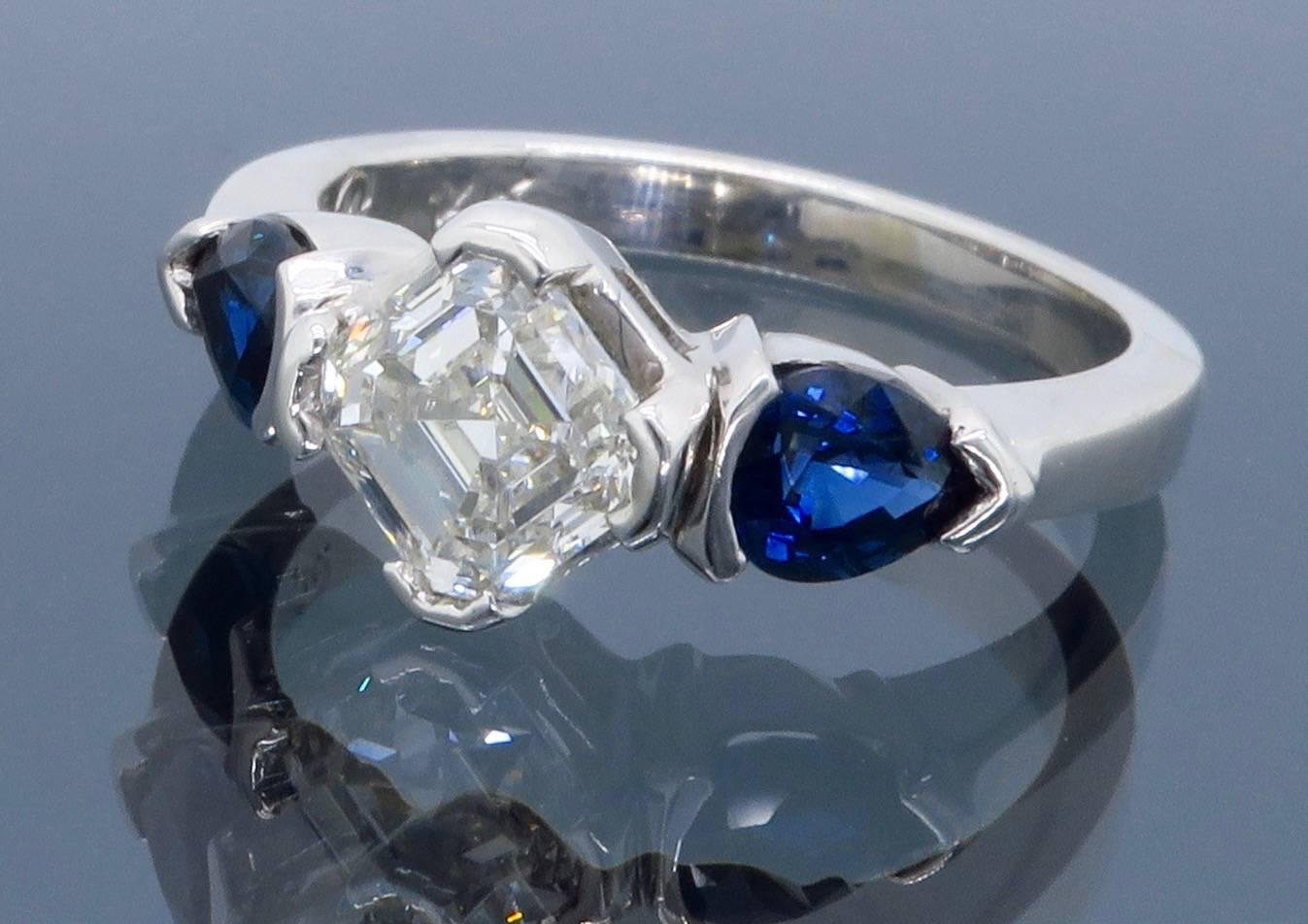 This beautiful ring features a .90CT Asscher Cut (Square Emerald cut) Diamond with G-H color, SI1 clarity. It is accented by two 4.9MM X 3.8MM pear cut blue sapphires. The 14K white gold ring is size 5.25 and weighs 4.1 grams.
