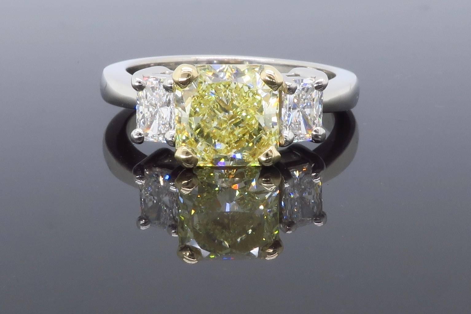 Platinum Three Stone diamond ring with a GIA Certified Radiant cut 2.08CT Fancy Yellow Diamond in the center with an impressive VVS1 clarity. There are two additional Radiant cut diamonds accenting the center stone weighing approximately .30ct each,