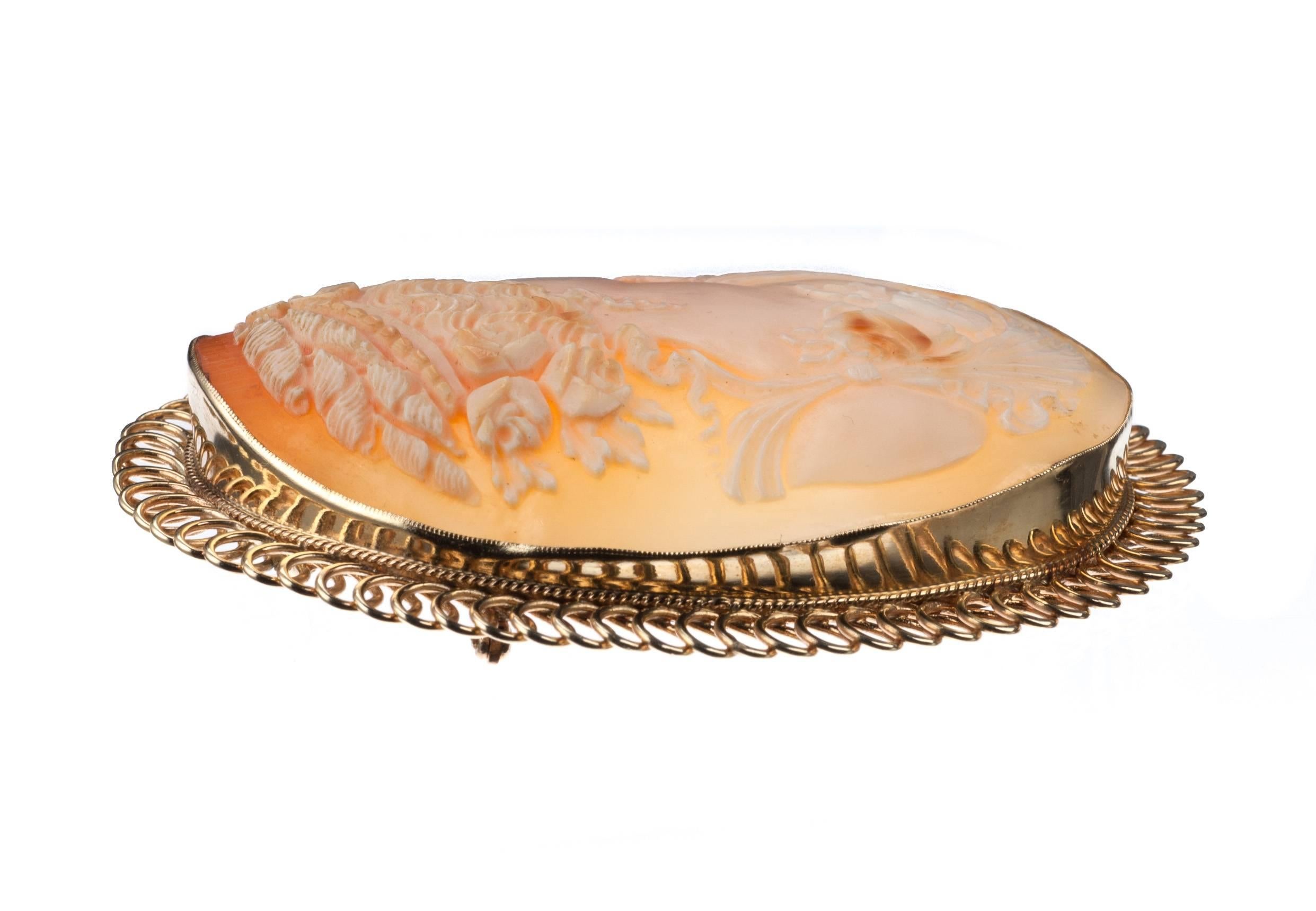 A shell cameo carved with a classic rubenesque portrait and framed in an ornate 14-karat yellow gold border that perfectly complements the rich warm oranges of the shell. Large yet lightweight, the cameo can be worn either as a pin or strung with a