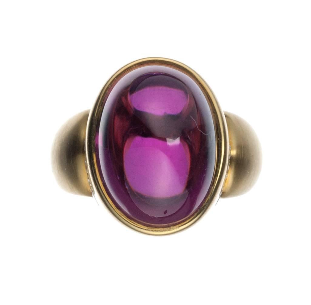 Almost elemental in its graceful, geometric curves, a rhodolite garnet ring from designer Susan Sadler. The high domed, oval cabochon rhodolite garnet, 17.51ct., is bezel set in satin-finished 18-karat yellow gold and accented with 14 brilliant-cut