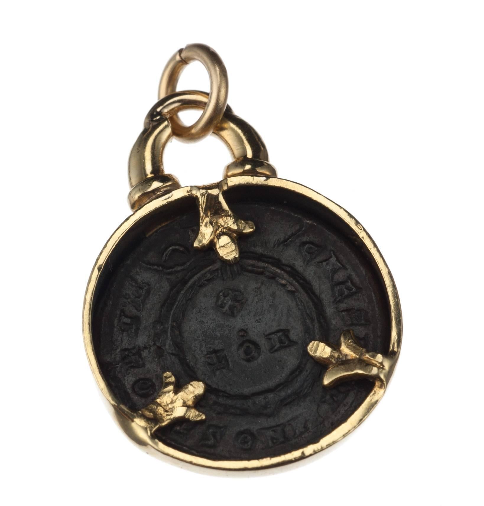 An 18-karat yellow gold charm featuring a bronze coin issued by the Roman empire that dates from the 3rd or 4th century A.D. The charm measures approx. 1.25” long and 0.75” in diameter.
