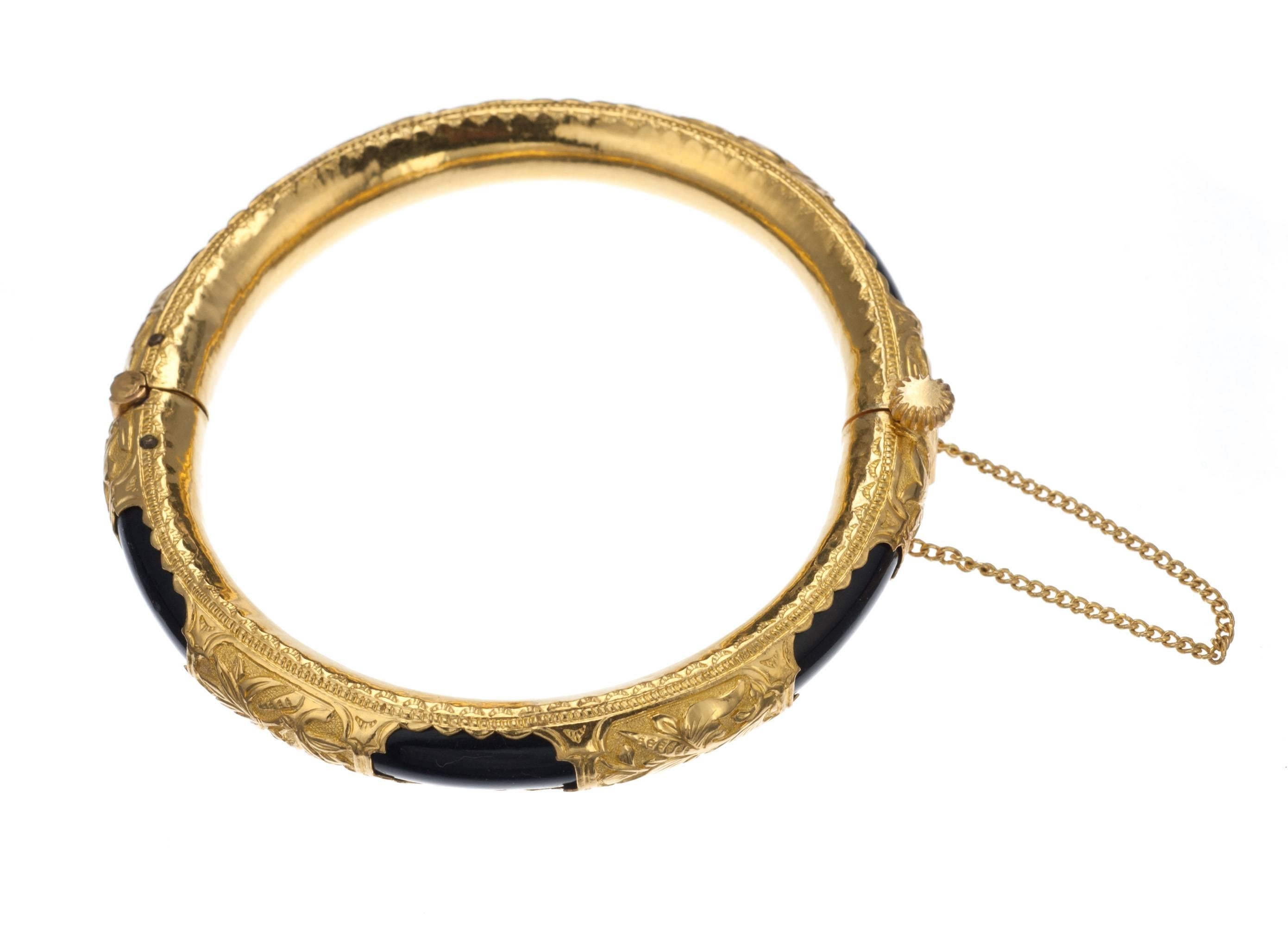 Fashioned from layers of 24-karat yellow gold and black onyx, a hinged bangle bracelet adorned with elaborate, classic floral motifs. Lightweight due to its clever construction, the bangle is fastened with a screw clasp and fitted with a safety