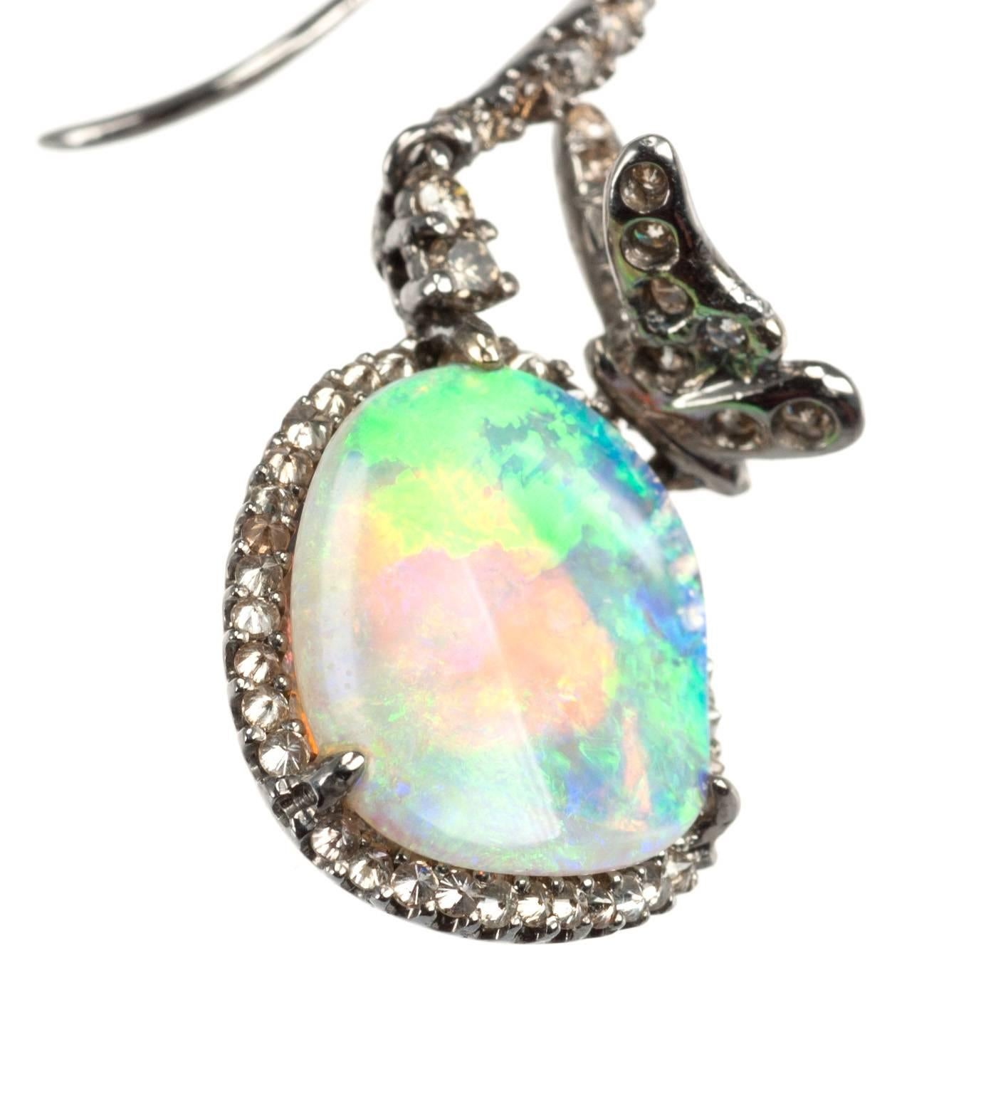 Two organically-shaped opals, weighing 4.22ctw., dangle from the ear with a fiery display of color. Flashes of pink, purple, green and yellow are framed by cognac diamonds weighing 1.04 ctw. Each 18-karat white gold earring is graced by a sparkling