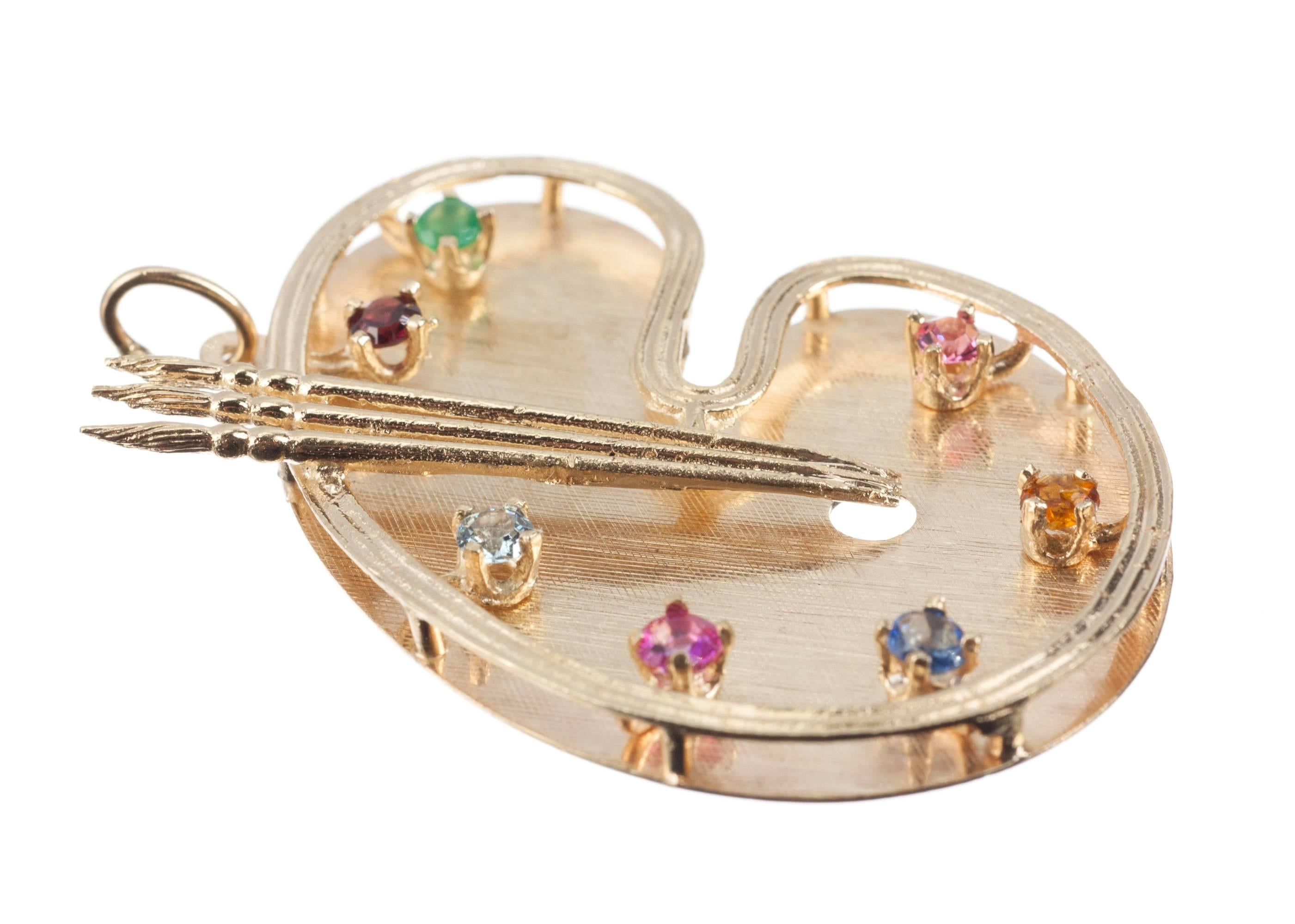 This magnificent, large 14-karat yellow gold charm resembling an artist’s palette is set with a collection of small colored gemstones, approx. 3.2mm each, including emerald, garnet, aquamarine, ruby, sapphire, citrine and pink tourmaline. Measuring