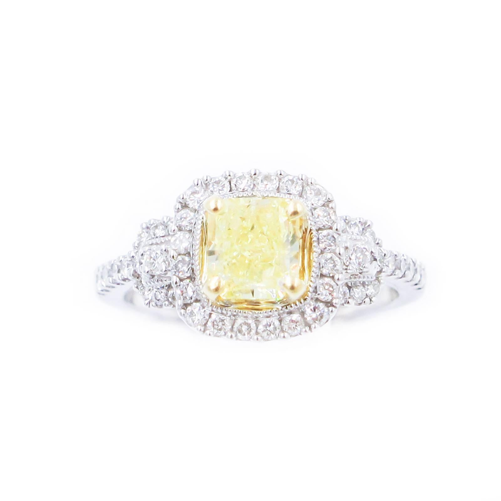 This very pretty halo ring features a center set Radiant Cut Fancy Yellow Diamond of .95 carat. The stone is rated Medium Strong Yellow intensity. The  surround contains 70 small VS-SI round, Brilliant Cut clear Diamonds running down the sides.