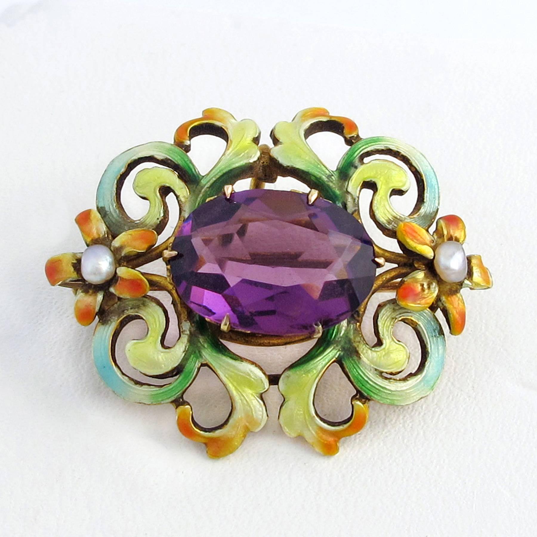A 19th century Art Nouveau pin is center set with a 13.00 x 9.30mm oval cut and faceted deep purple Amethyst in an elaborate mount. The  Verre Emaille in predominant shades of green, blue, yellow and orange is beautifully rendered and detailed with