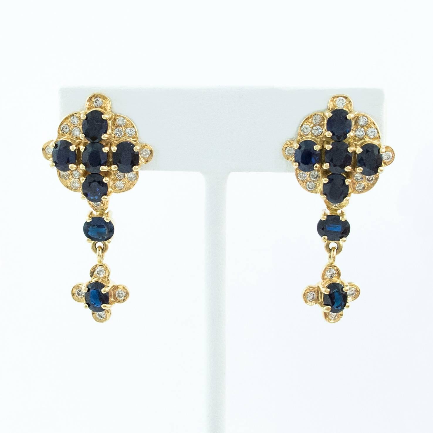 A lovely pair of 14K yellow gold Blue Sapphire and Diamond Gold Cross Drop Earrings. Set with fourteen Oval Faceted natural Blue Sapphires and forty Brilliant cut Diamonds.

The earrings hang 1.75 inches long. The top of the earrings sit well on the