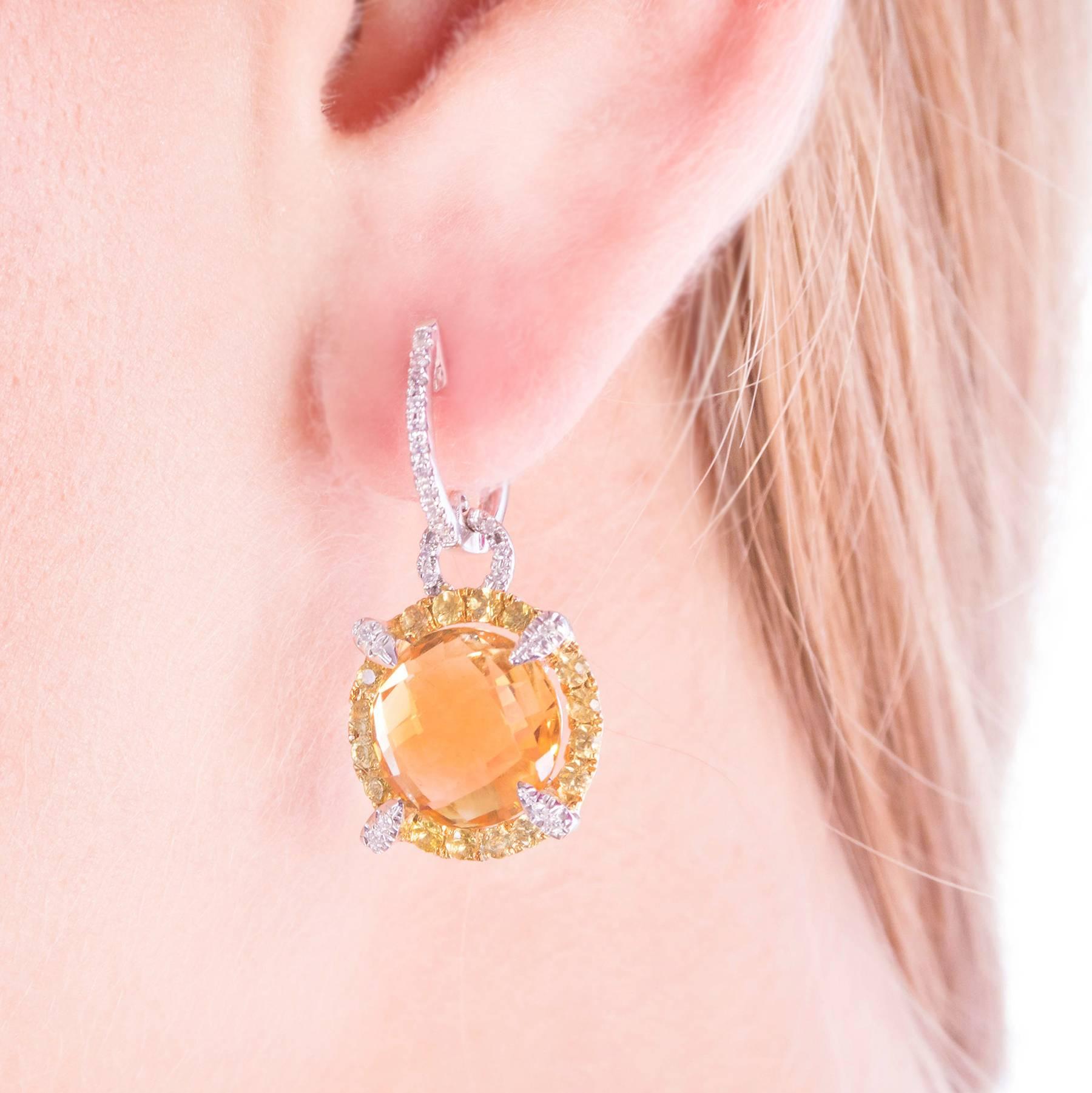 These pretty 18 Karat White Gold and Diamond Earrings are center set with round, faceted Citrines measuring 10.80 mm, equaling approximately 4 carats each. The Citrines are surrounded with bead set Yellow Sapphires/Corundums accented with and