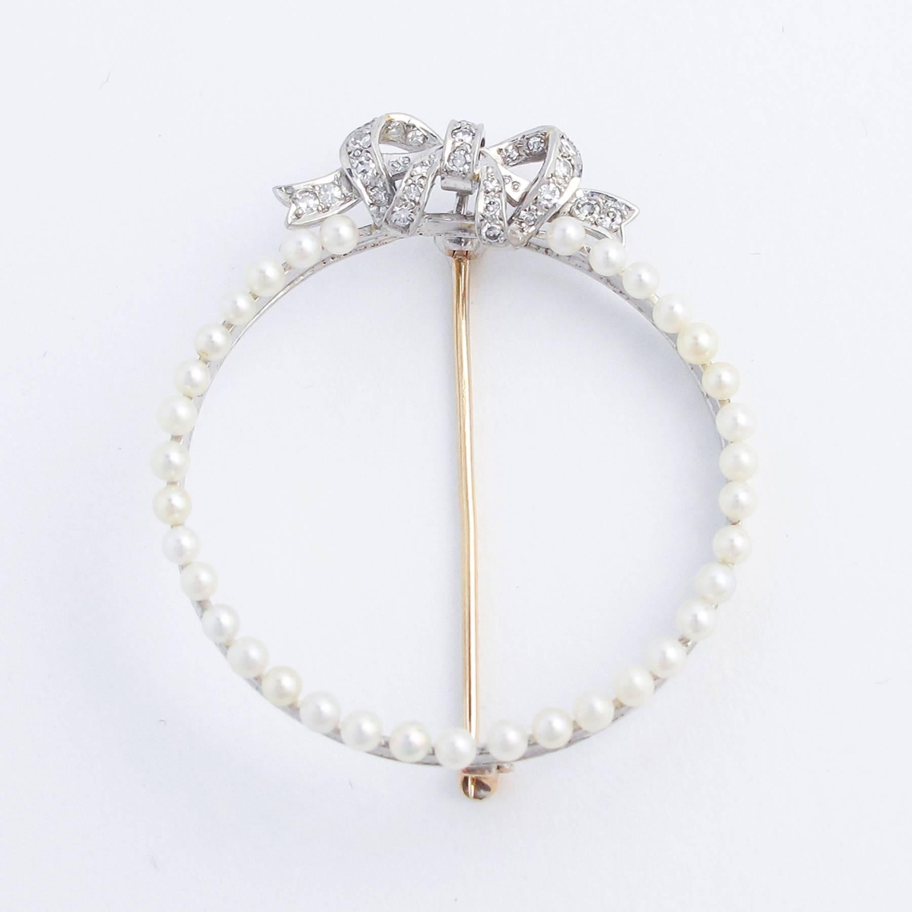 Natural Silver Gulf Pearls are peg set in a circle and tied with a pretty Diamond set Bow comprised of 35 Diamonds.

Very wearable at 1.75 inches across, and light weight at 5 grams. Typical of the period, the White Gold is 18K while the broaching