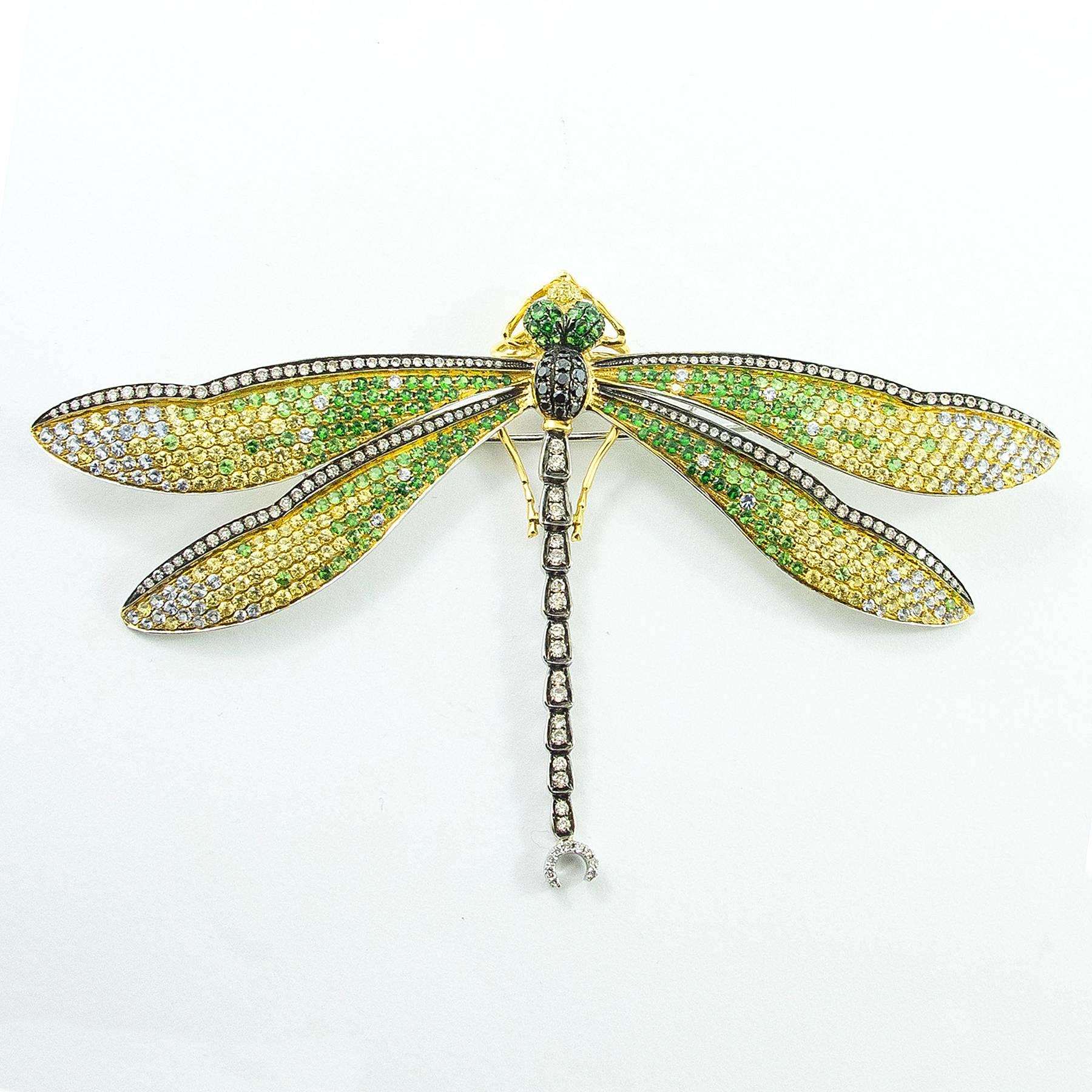 A large and exquisite Diamond, Sapphire and Tsavorite Garnet Dragonfly brooch is pave and bead set with 638 clear and colored Diamonds, multi colored Sapphires, Corundums and Tsavorite Garnets in a hand assembled 18K gold mount. 

The brooch
