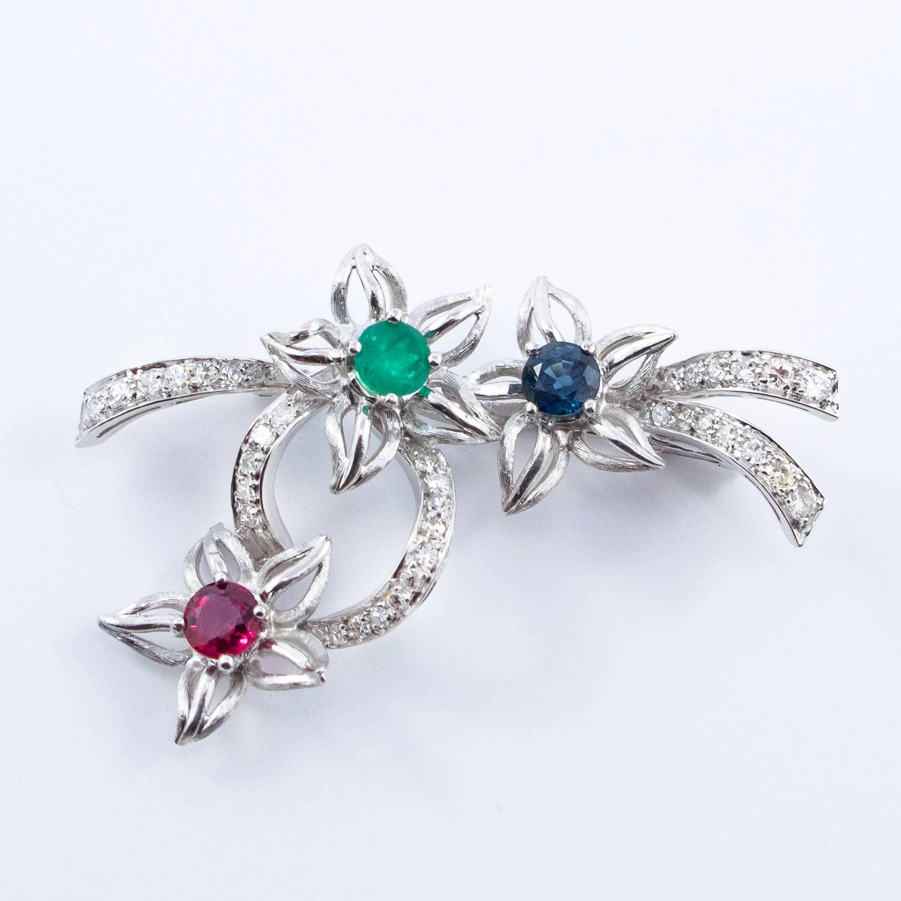 A beautiful Diamond set Platinum brooch dates to about 1940 and consists of a ribbon of Diamonds with a spray of 3 open flowers, set with round, faceted precious gemstone throat of about .50 carat each including one Emerald, one Blue Sapphire and