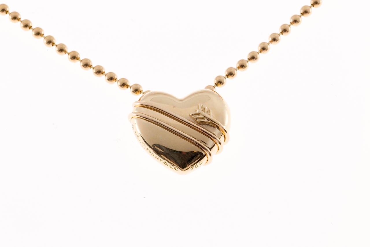 1994 Tiffany & Co. 3 dimensional solid 18k yellow gold heart with an arrow wrapped around. Heart slides on chain. Retired model. 

18k Yellow Gold
Top to Bottom: 18.32mm or .72 inches
Width: 20mm or .80 inches
Depth or Thickness: 9mm
20.5