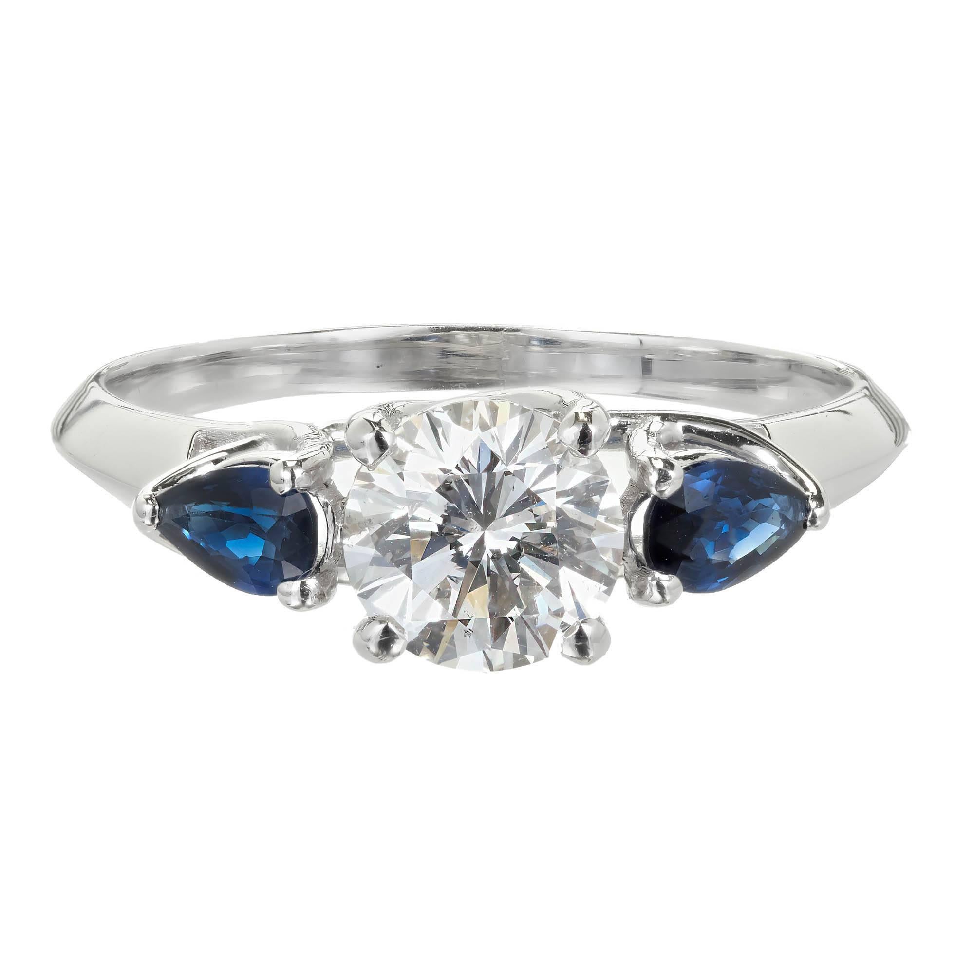Peter Suchy custom made diamond and sapphire engagement ring with a bright white sparkly center Diamond and 2 pear shaped bright blue Sapphires side diamonds in a simple but very different crossed prong three-stone platinum engagement ring. 

1